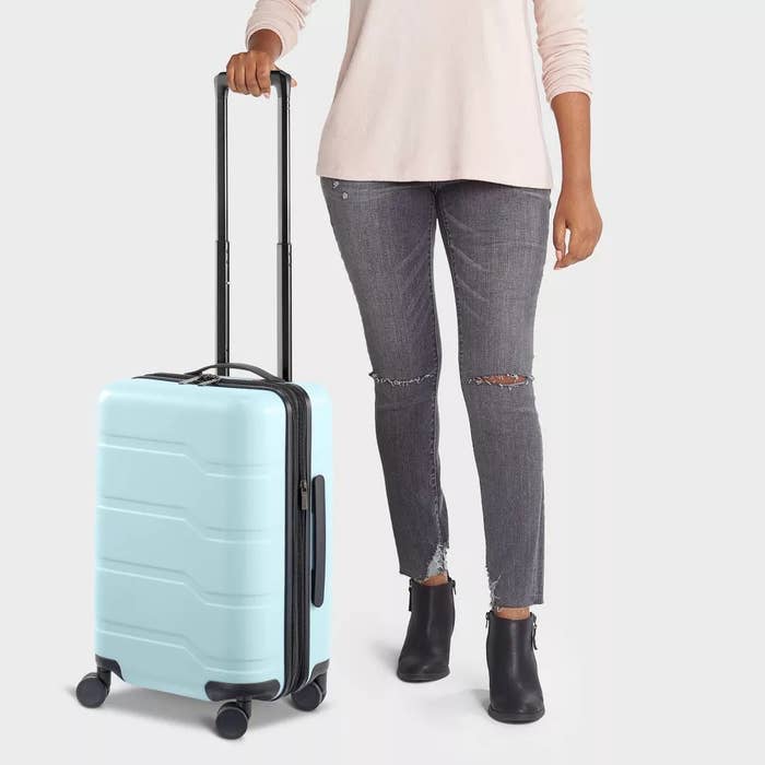 model adjacent  to a airy  bluish  hard   ammunition  rolling carry-on suitcase