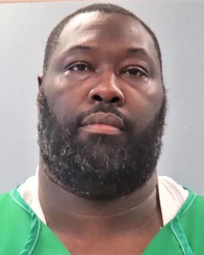 A idiosyncratic with a beard wearing a greenish top, facing the camera with a neutral expression