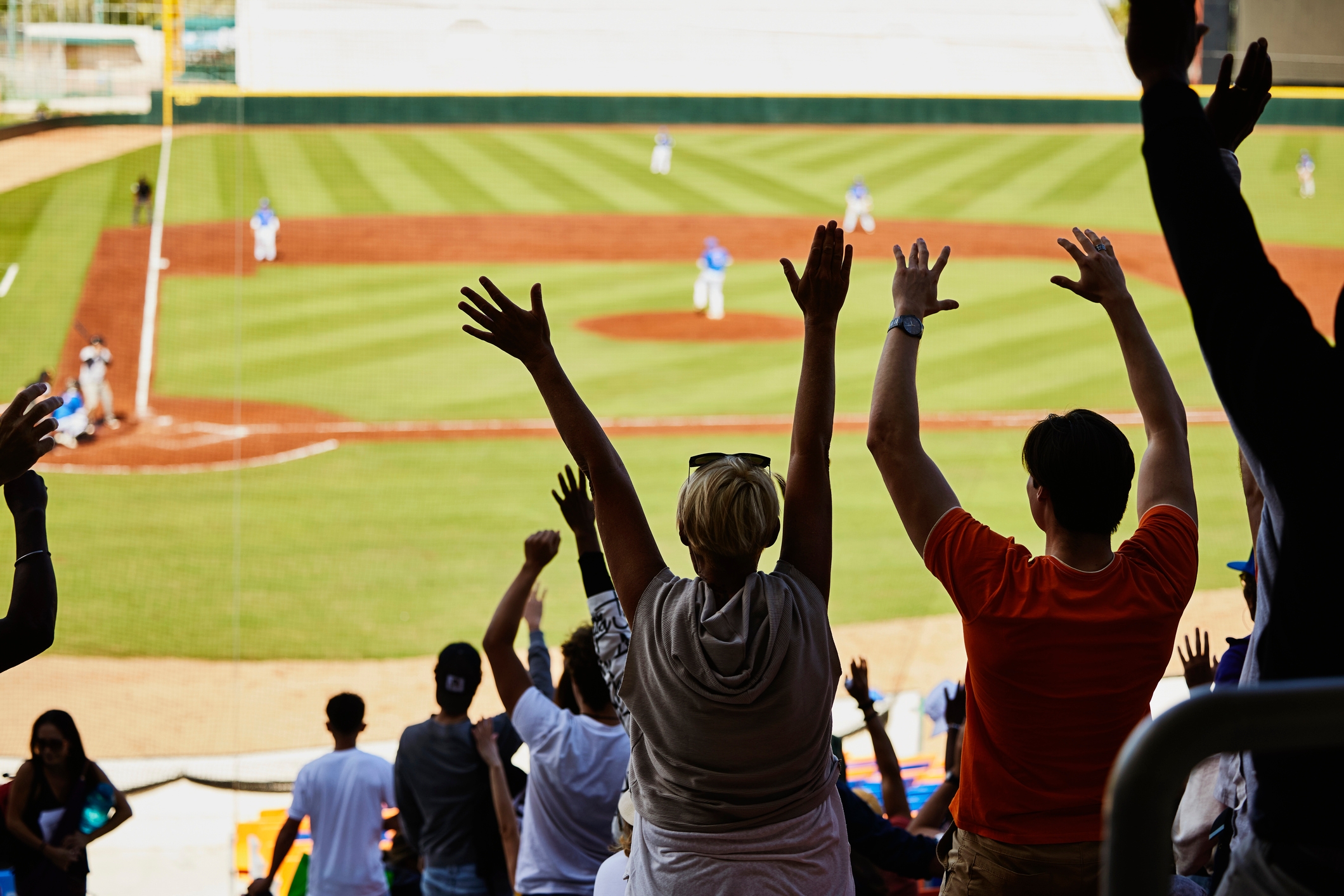 Fans heier med hevede våpen på et baseballkamp og ser på spillere på banen. Atmosfæren er livlig og energisk
