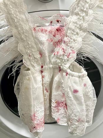 White lace dress with feather details stained with red marks, draped over a washing machine