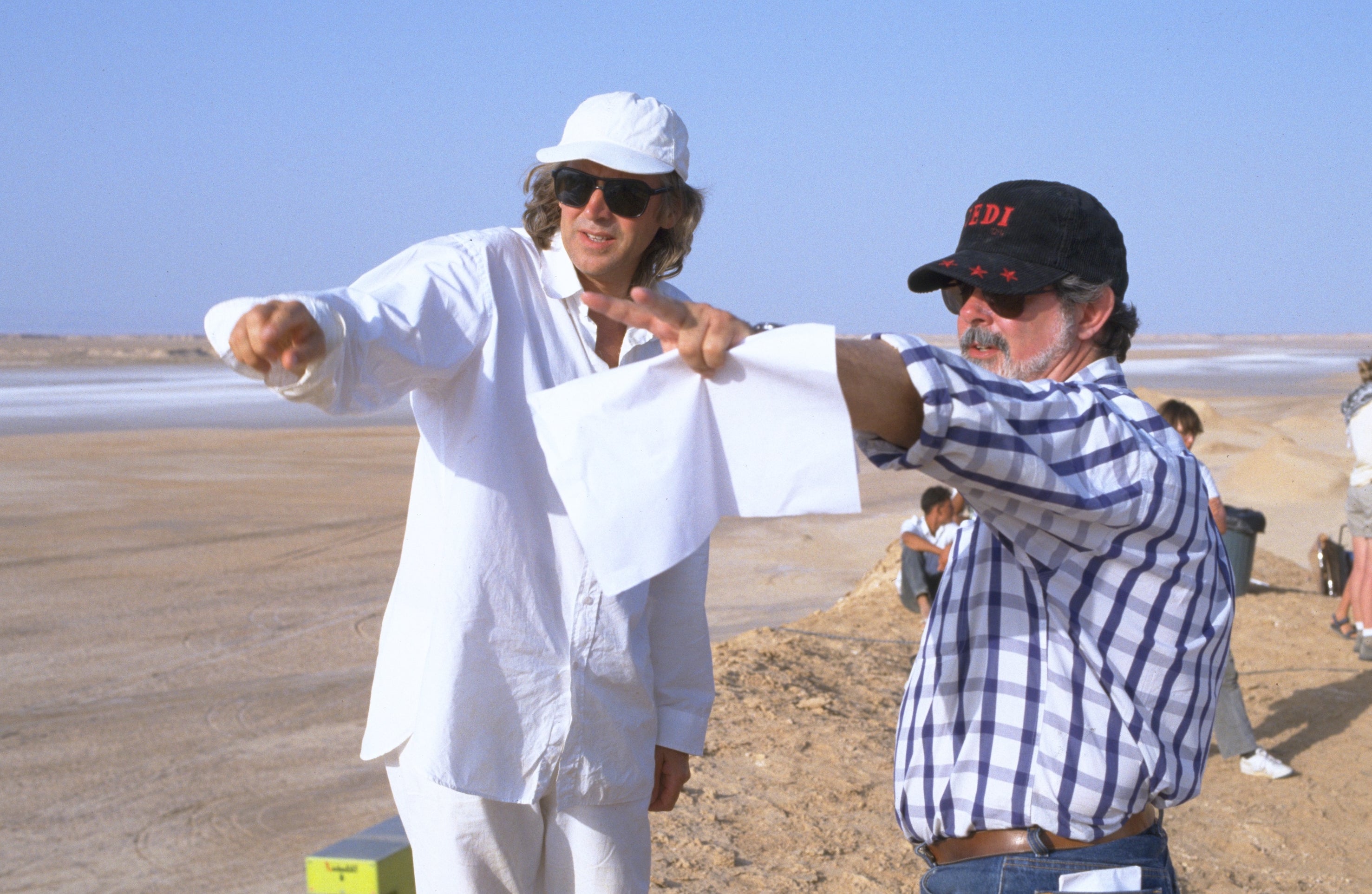 Two filmmakers in casual attire discuss a scene in a desert location, with one pointing in the distance