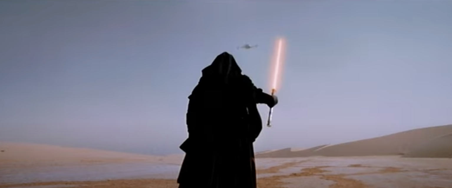 Silhouetted figure in a cloak holding a lit sword against a desert landscape, with a distant flying object in the sky