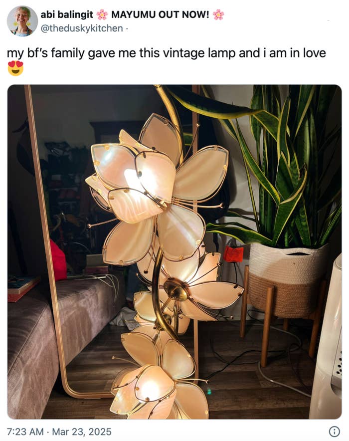 Lampu bunga vintage dengan kelopak bercahaya ditampilkan di samping tanaman tinggi di ruangan yang nyaman. Judul mengungkapkan cinta untuk hadiah itu