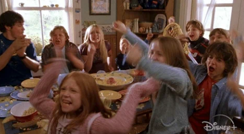 Children cheer and throw popcorn in the air during a playful meal at a dining table in a home setting
