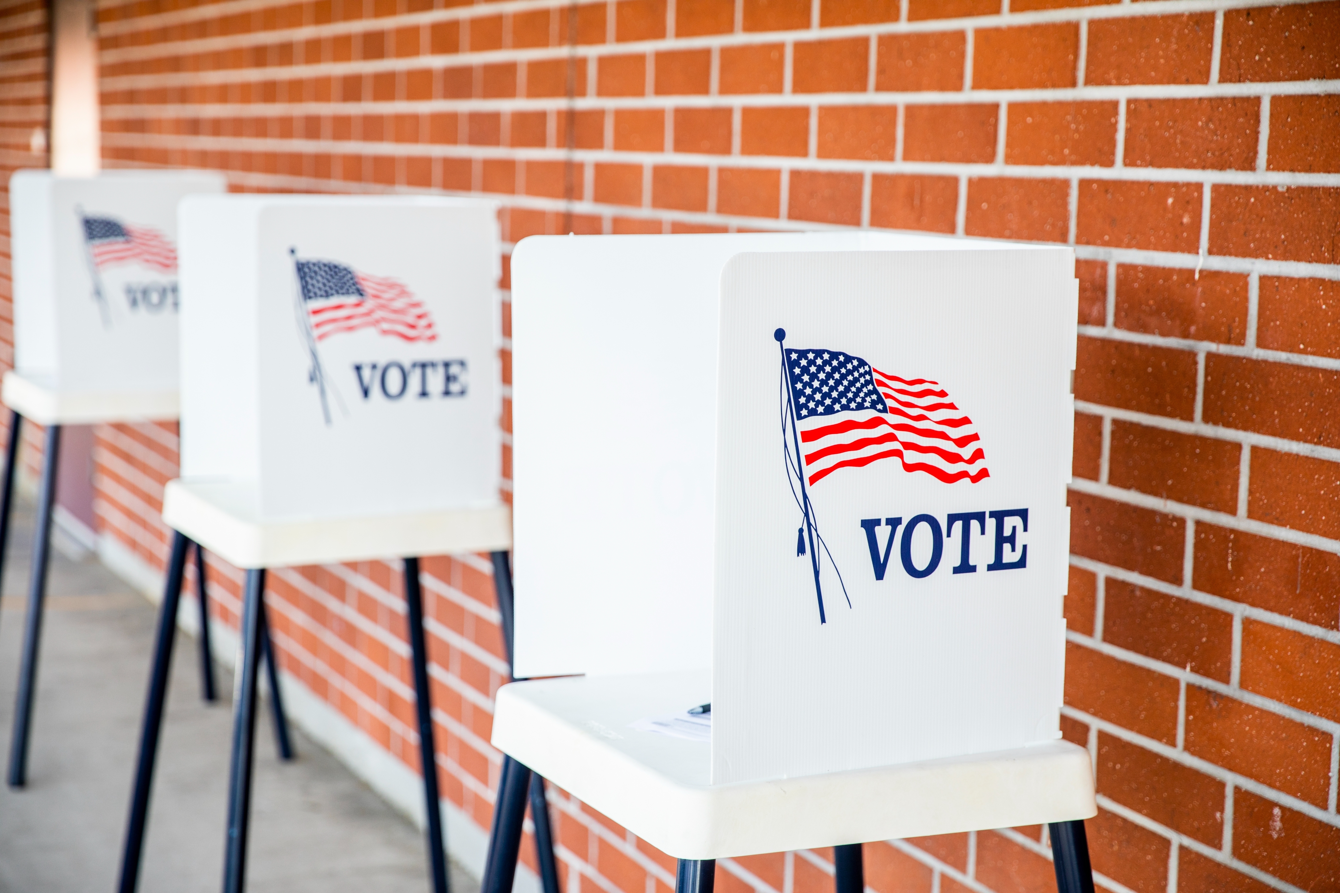 Voting booths lined up outside a brick building, each with an American flag and the word &quot;VOTE&quot; on them.