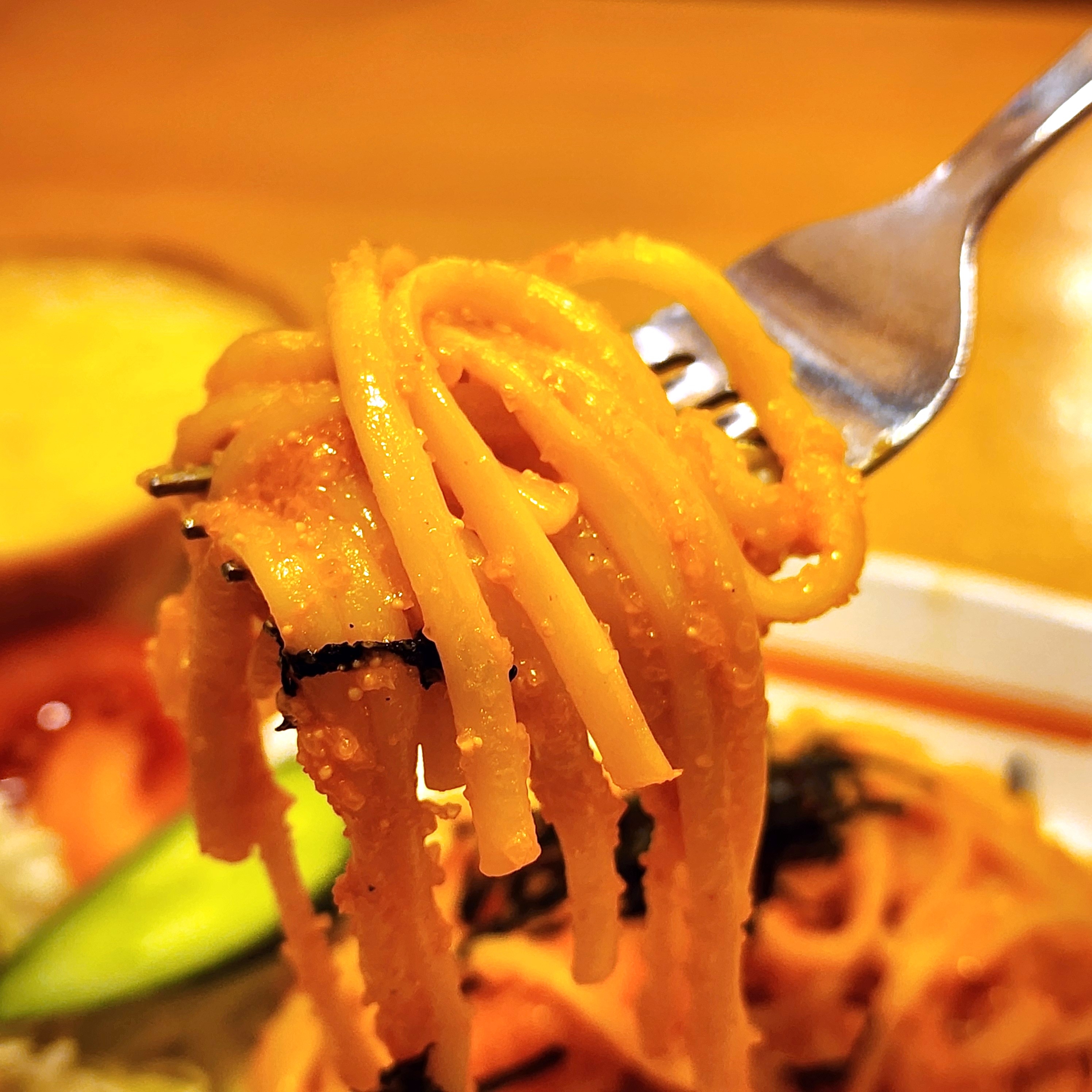 フォークで持ち上げられたクリーミーなパスタのクローズアップ。背景にサラダとパンが見える。