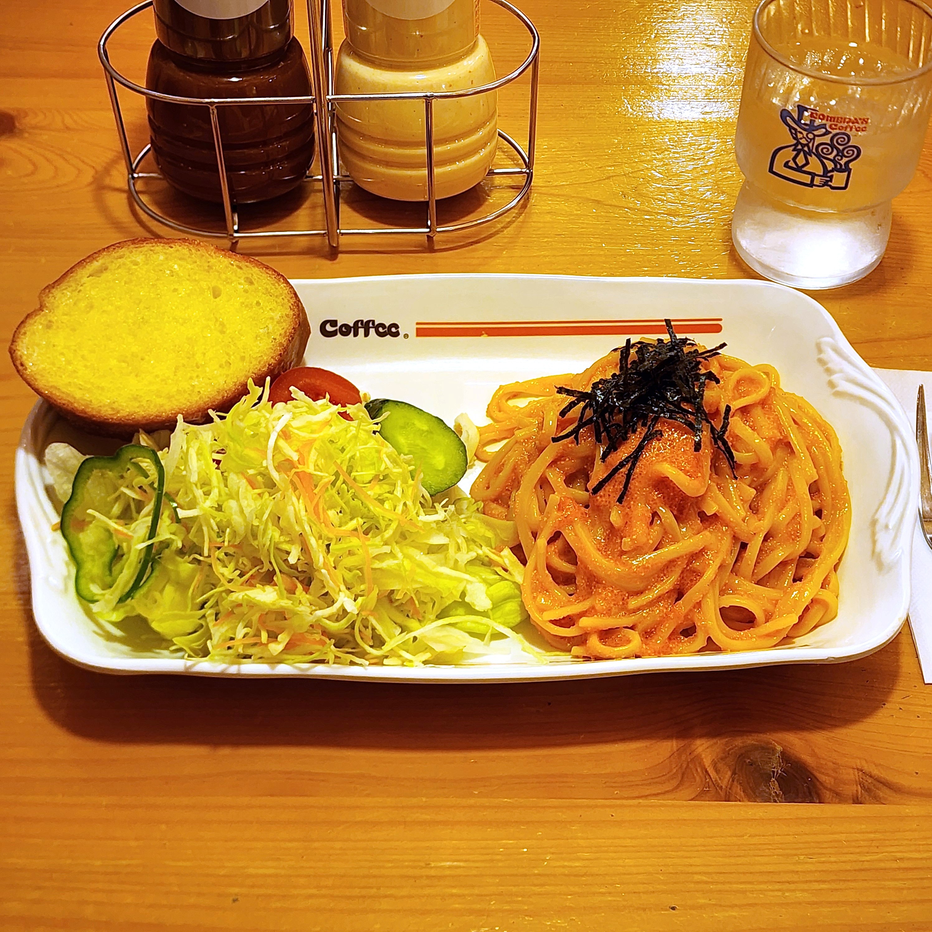 テーブルの上に明太子パスタ、サラダ、ガーリックトーストが乗った皿。隣に調味料と水のグラスがある。