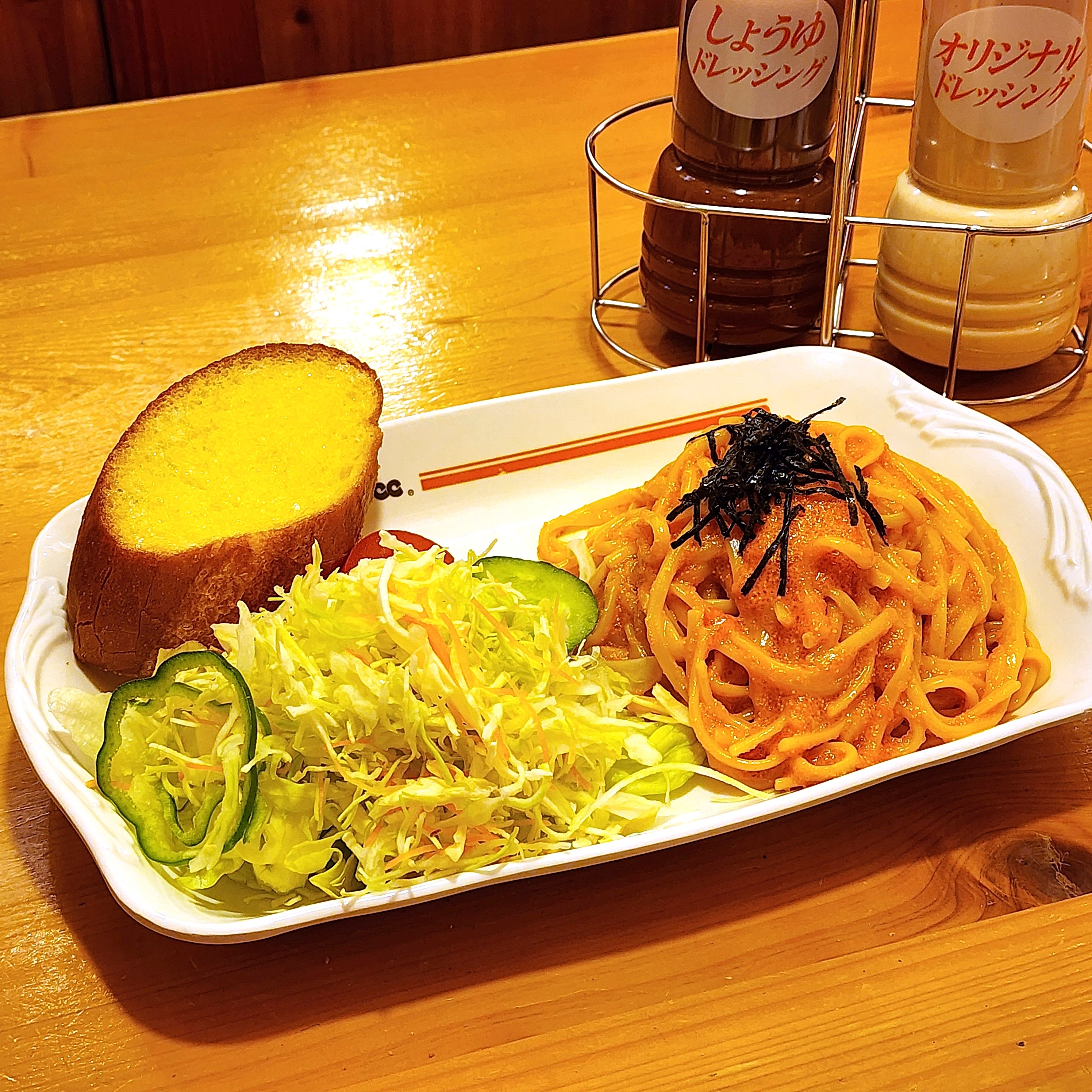 パスタ、キャベツサラダ、ガーリックトーストが白い皿に盛られ、ドレッシングが後ろに置かれているレストランの食事。