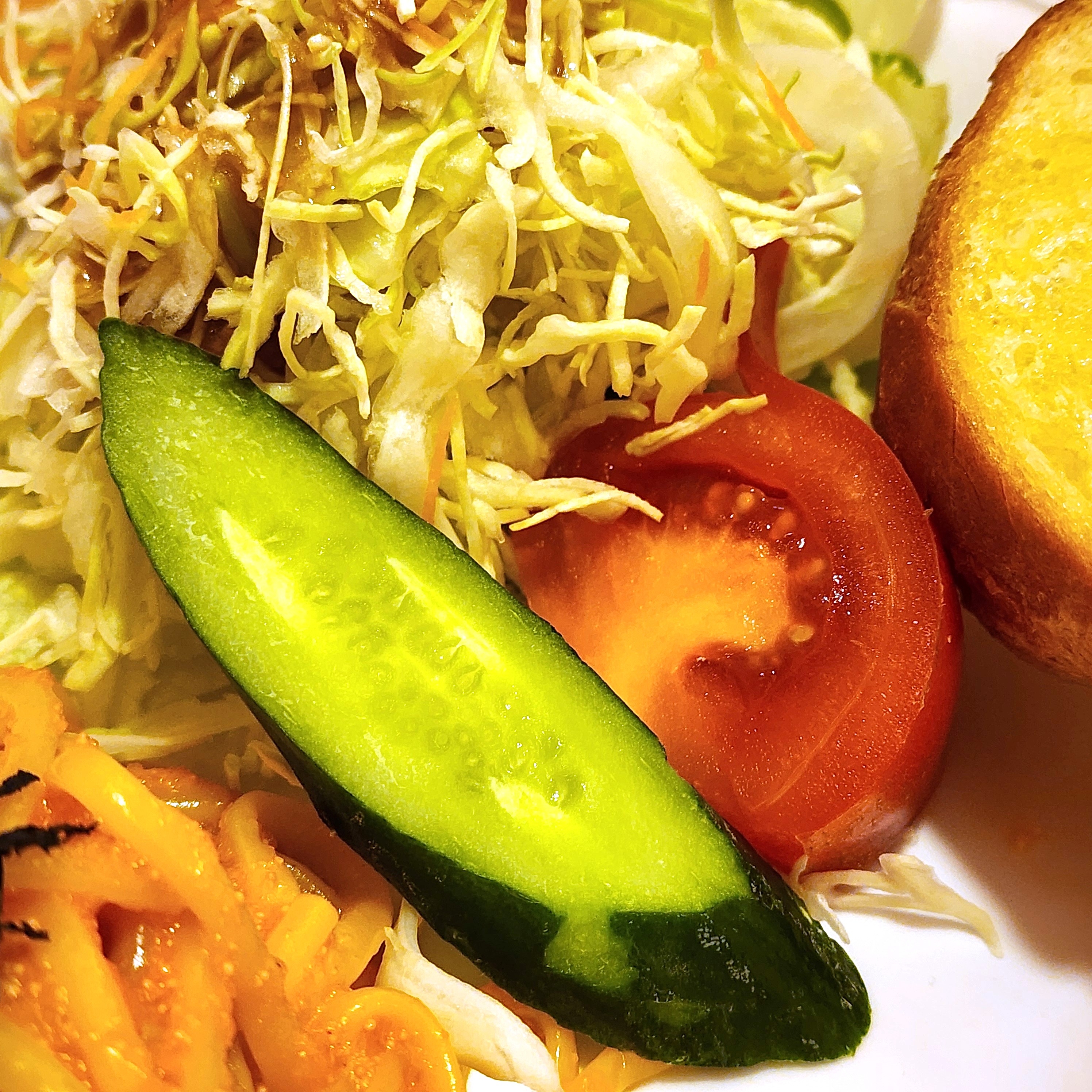 サラダのプレートに野菜とパン。キャベツ、トマト、キュウリのスライス、隣にはパンが添えられています。