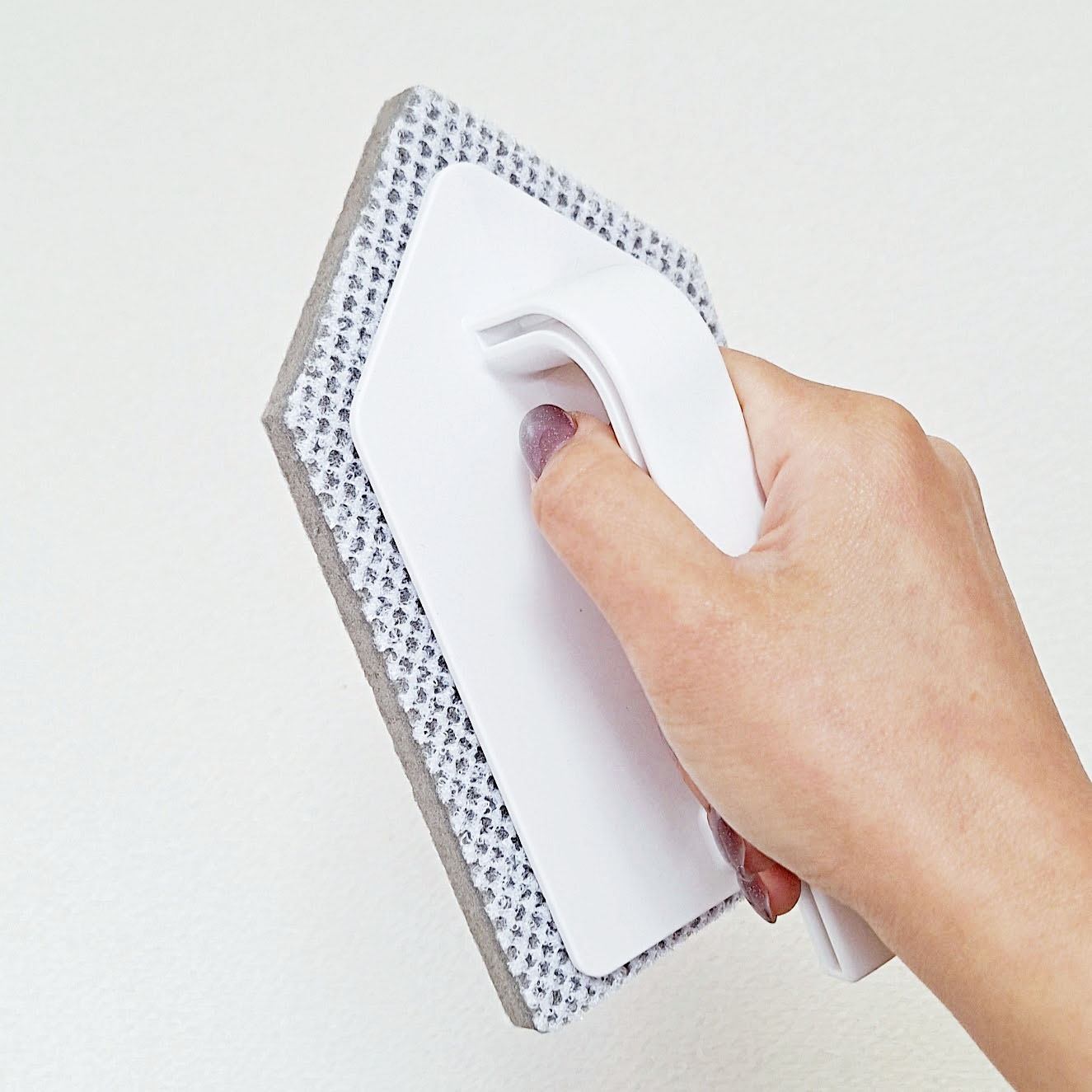 壁にスポンジ付きクリーナーを押し当てている手。シンプルで効果的な掃除ツールの使用法を示しています。