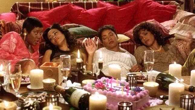Group of four women reclining on a couch, surrounded by candles and a decorated cake, in a relaxed and celebratory setting