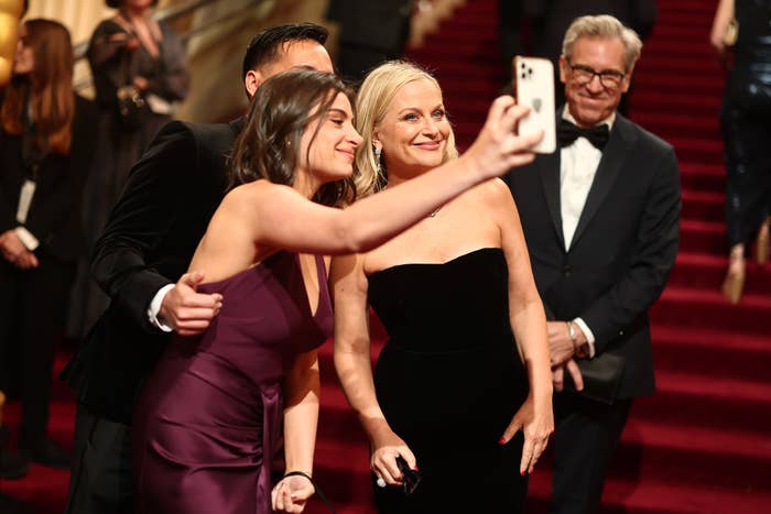 Group of celebrities in formal attire taking a selfie on a red carpet