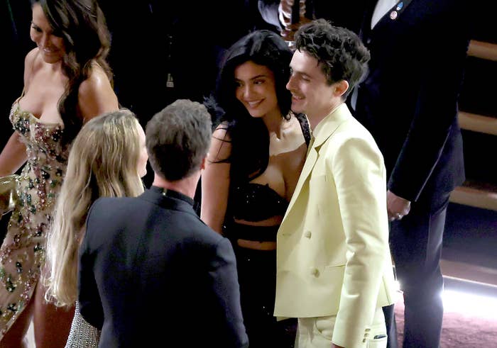 Kylie Jenner and Timothée Chalamet  conversing at the Oscars. Kylie wears a strapless black dress; Timothee a yellow suit