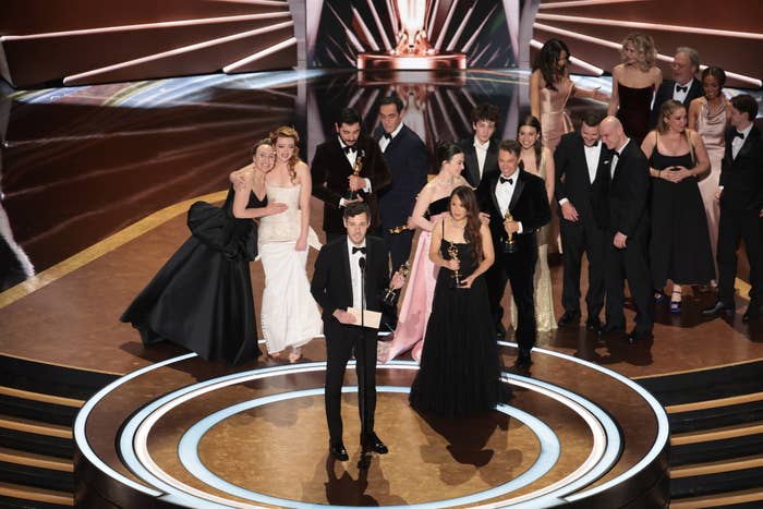 A group of elegantly dressed celebrities, many holding awards, standing on stage at the Oscars