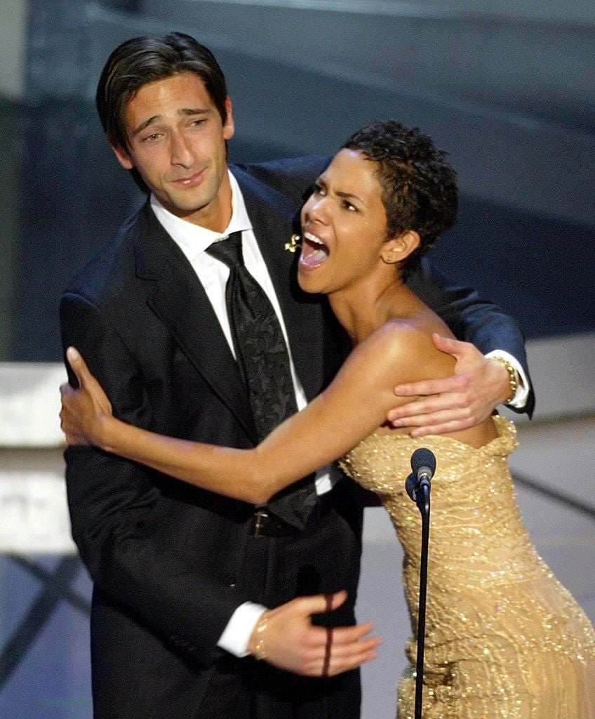 Man in suit embraces woman in strapless gown on stage, both smiling