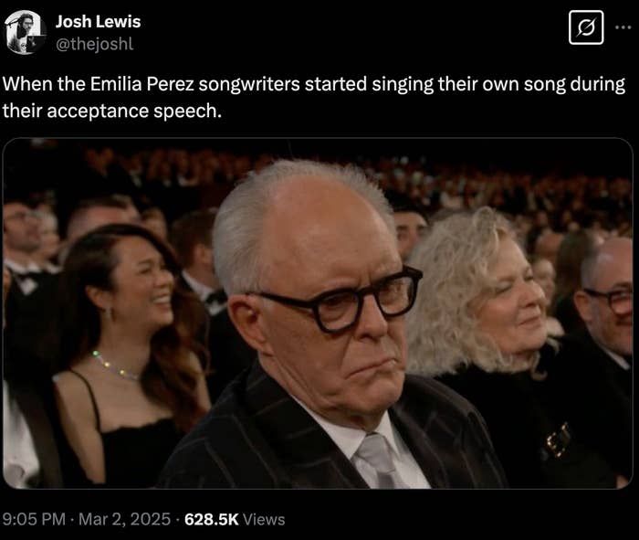 John man in glasses, seated in the audience, looks unimpressed. tweet: