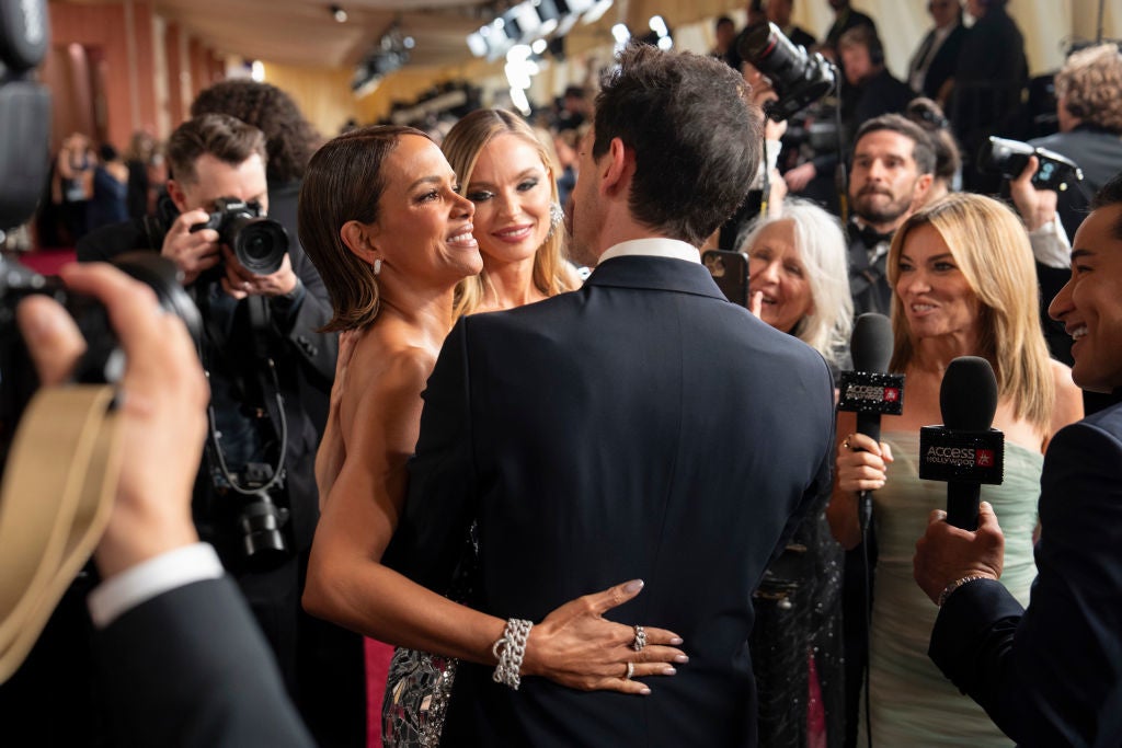 Guests on a red carpet pose for photos amidst a crowd of photographers and interviewers
