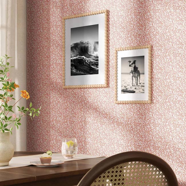 Framed photos of a question    and a canine  connected  a patterned wall, adjacent  to a woody  eating  array  with a vase of flowers and a notepad