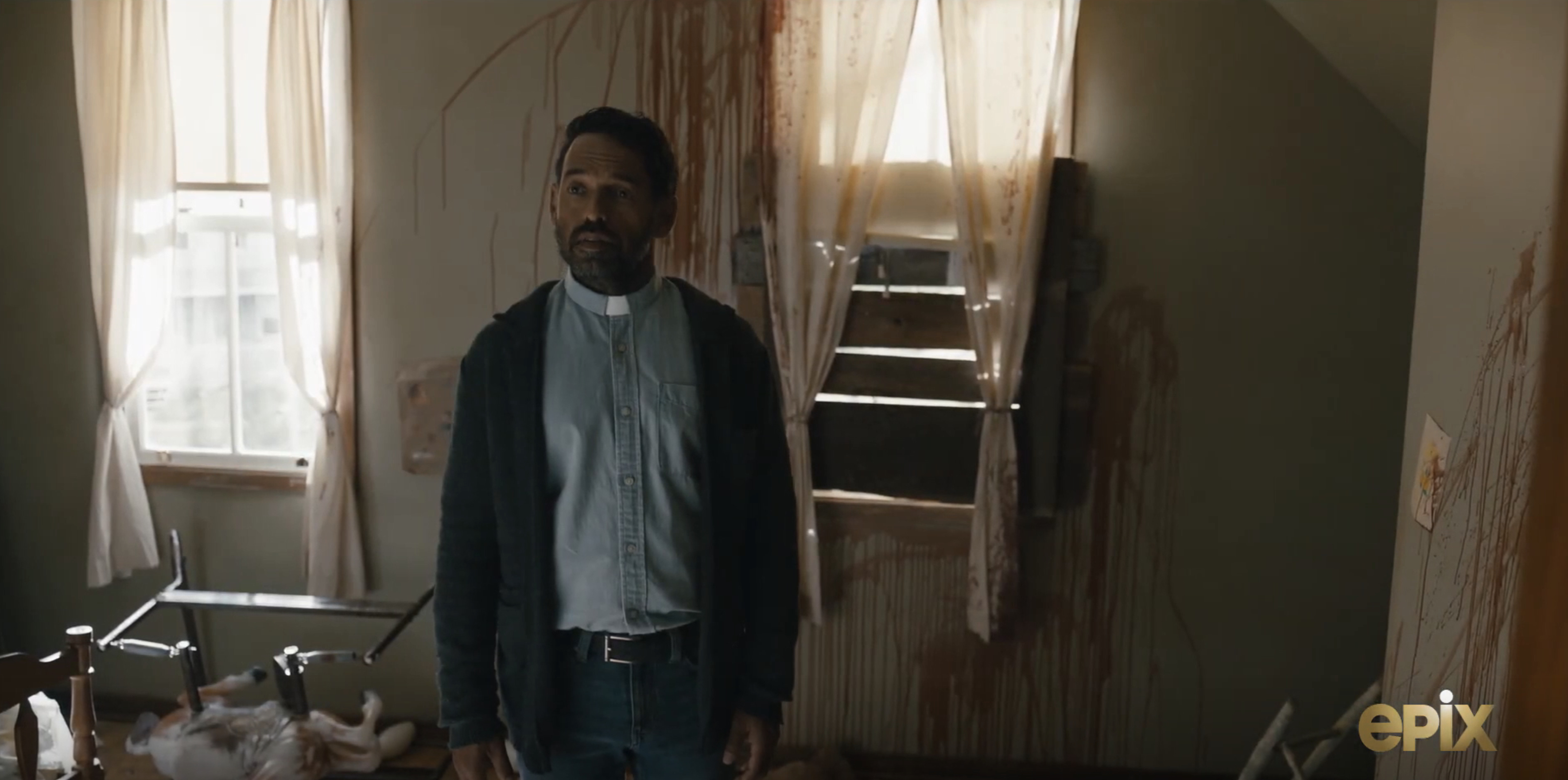 In a scene from &quot;From,&quot; a priest stands in front of a wall covered in blood