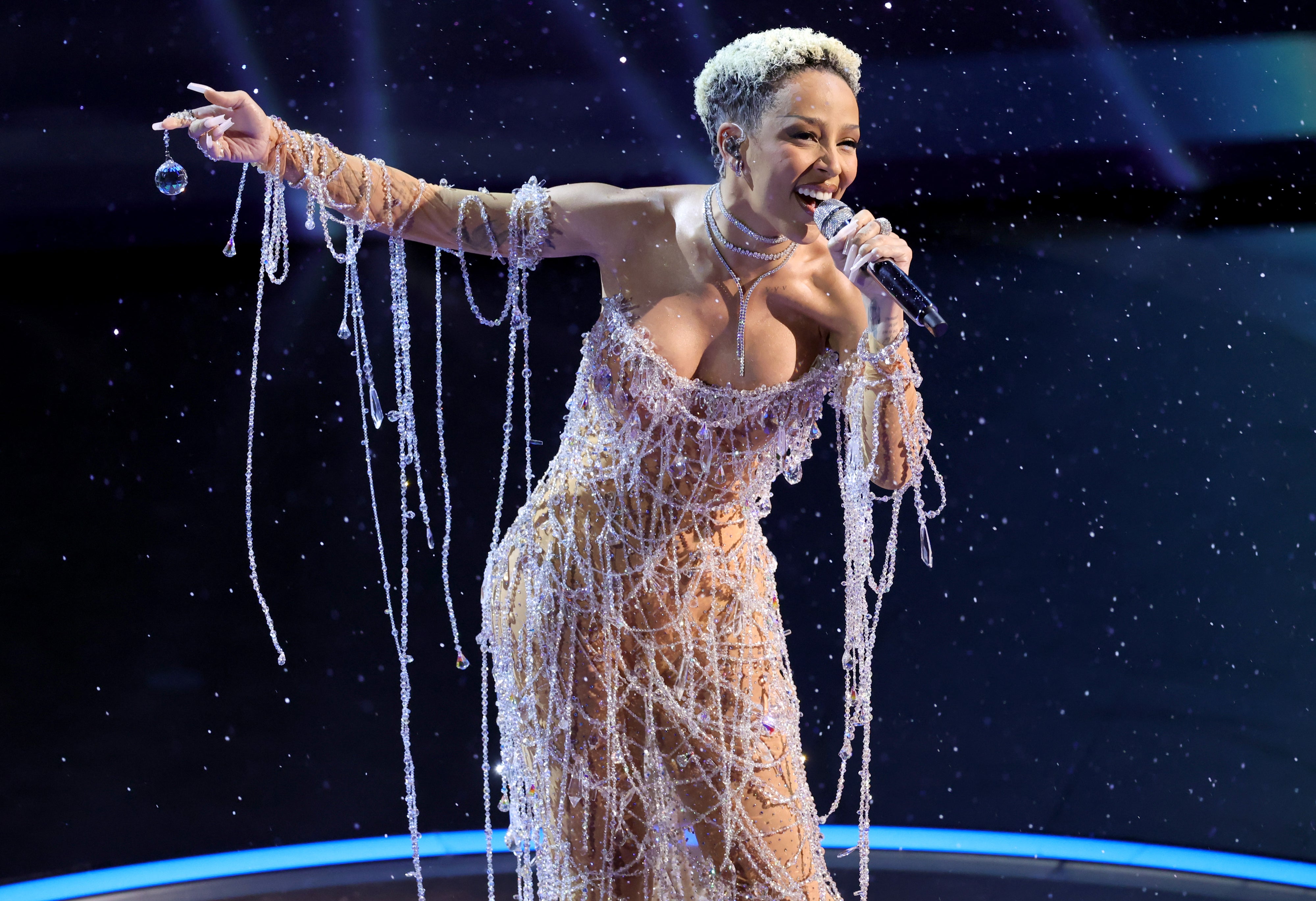 Person on stage wearing an elaborate, beaded gown, holding a microphone mid-performance