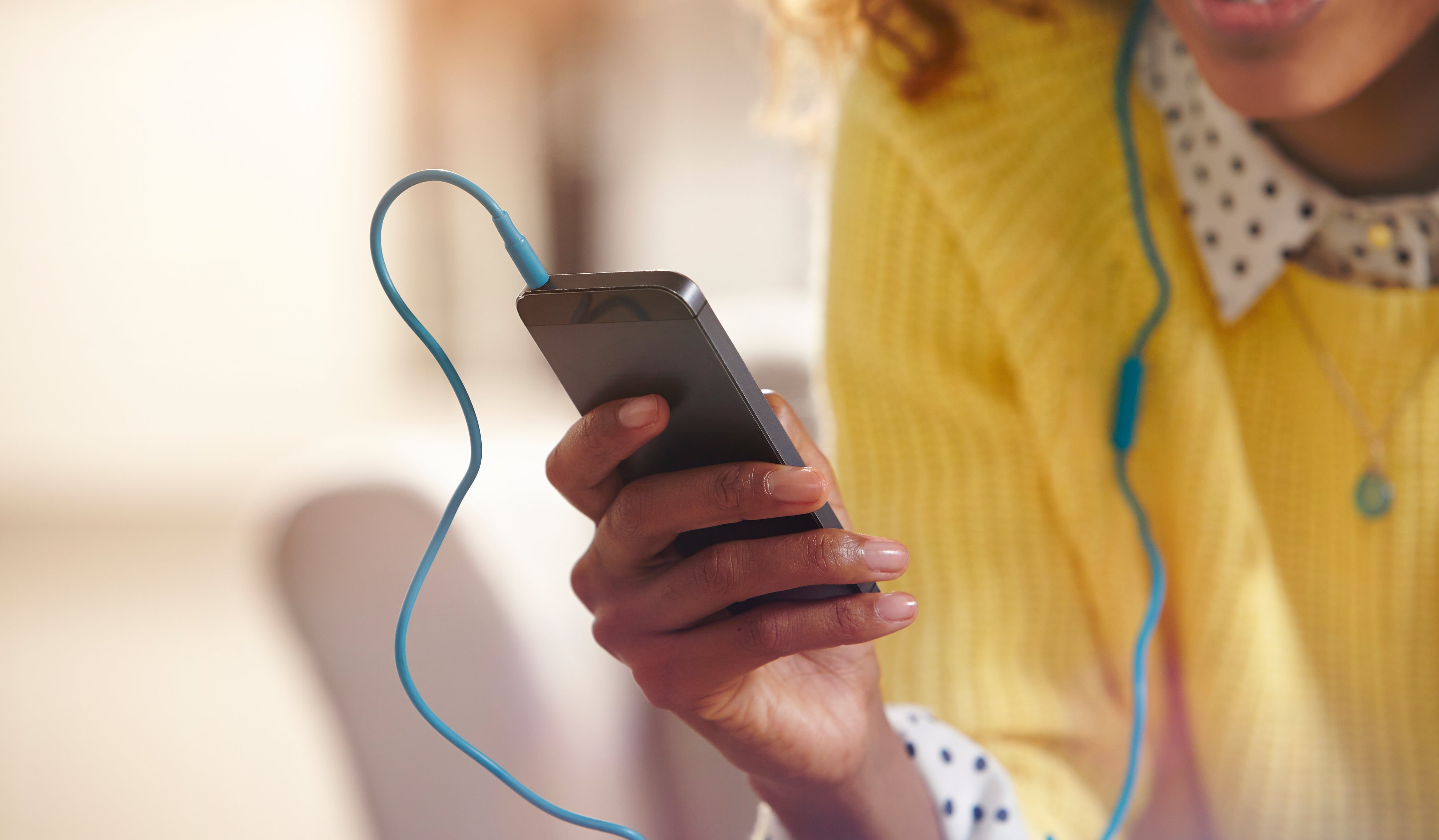 Person som har på seg en gul genser bruker en smarttelefon med øretelefoner, ser opp engasjert og innhold