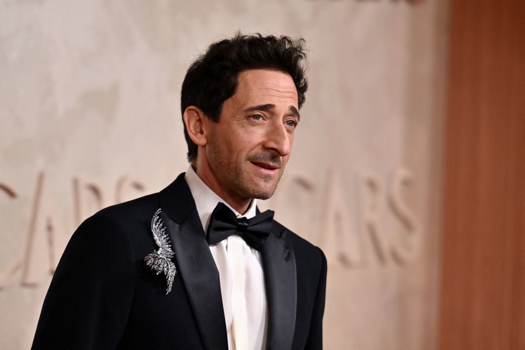 Man in formal suit with bow tie and feathered brooch attends a celebrity event