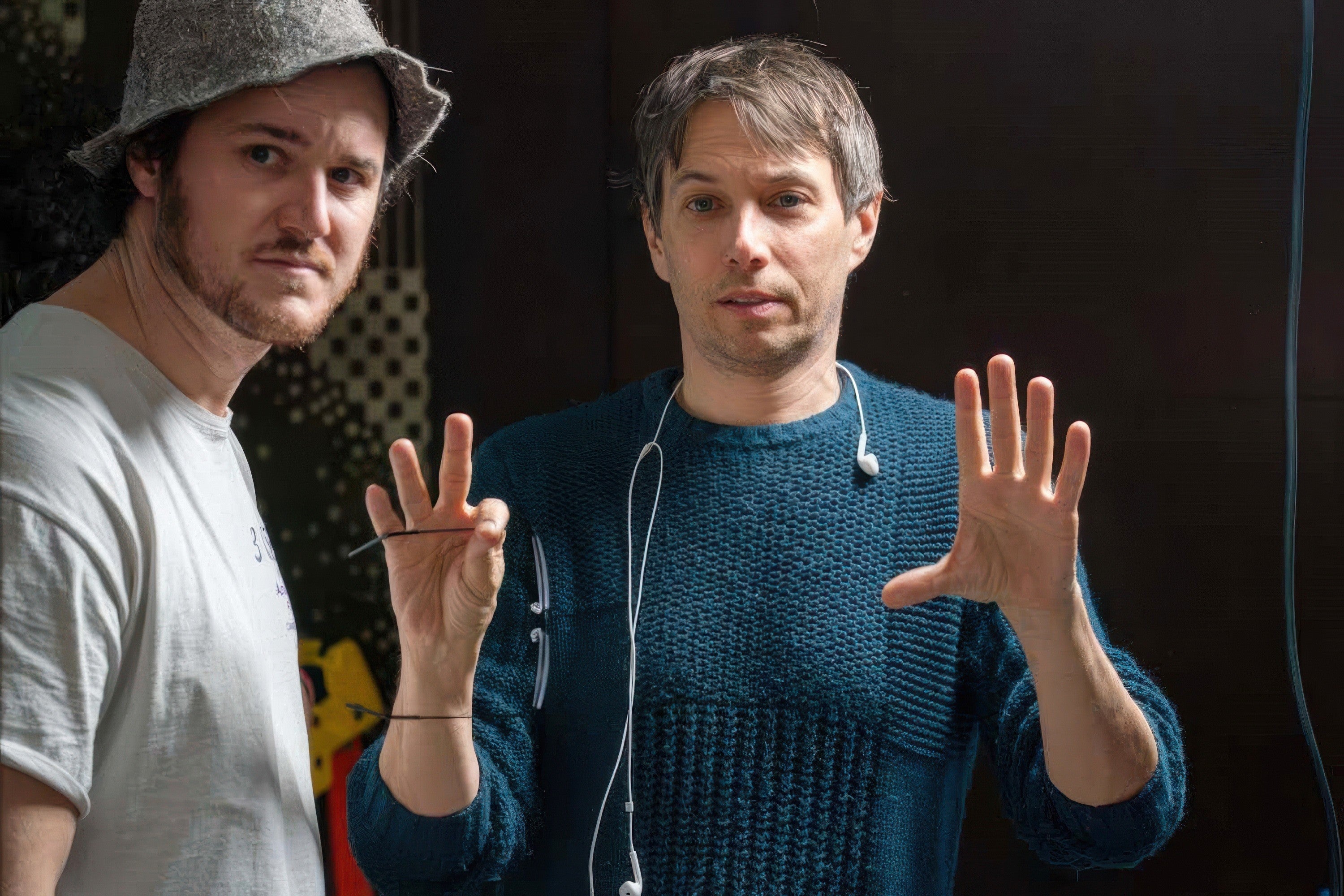 Two individuals on a film set, one holding a script and the other gesturing with hands, wearing casual attire