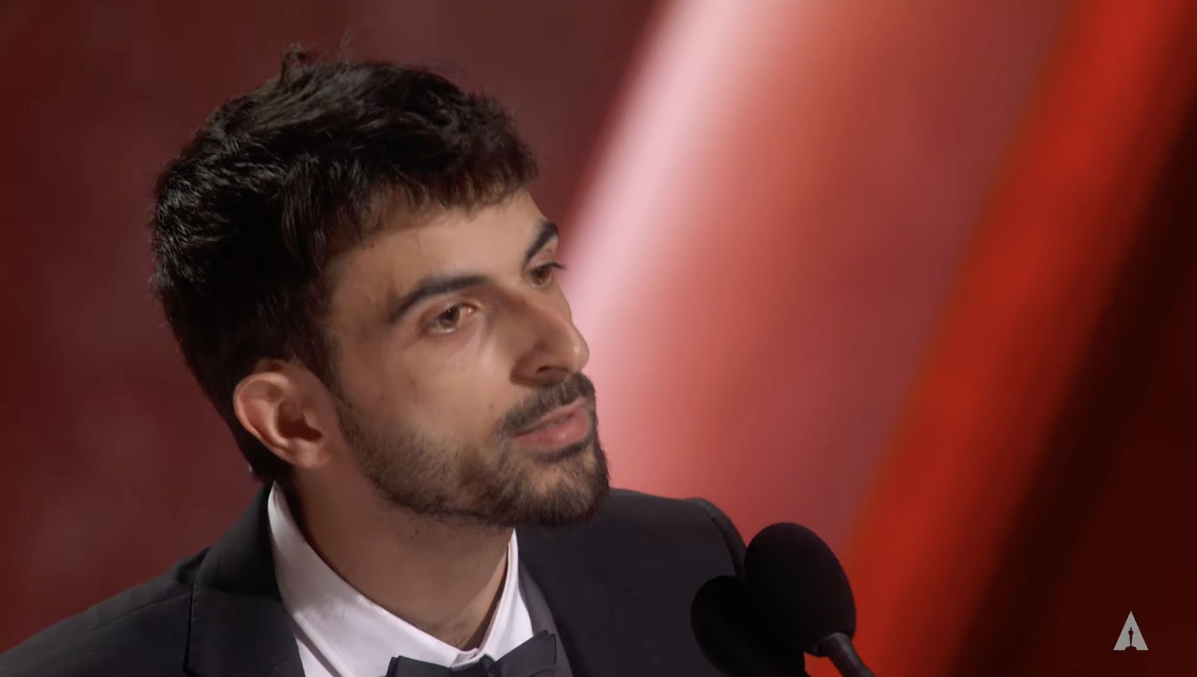 Person in a suit and bowtie speaking at a microphone during an event