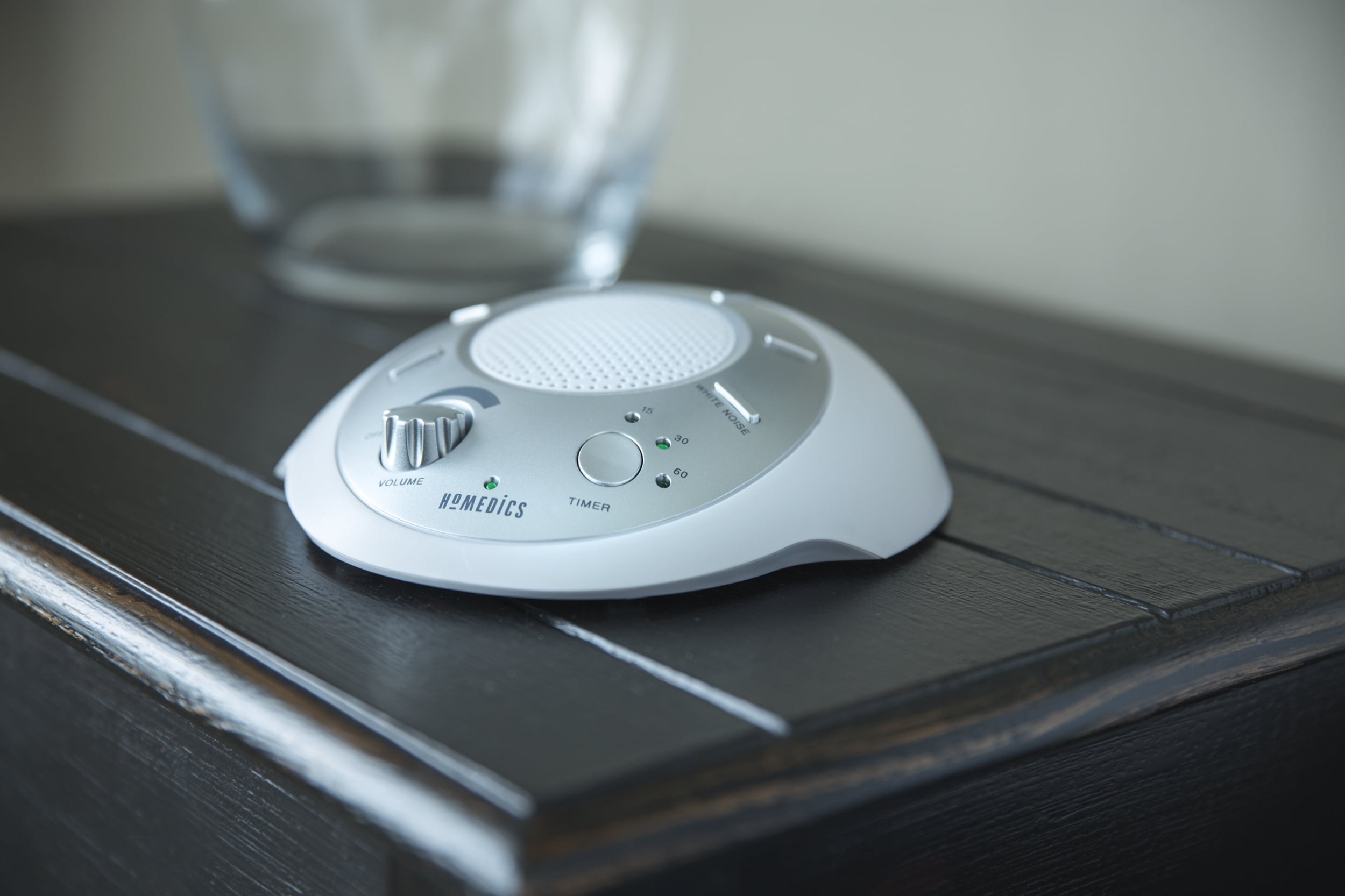 White noise machine on a bedside table, featuring volume control knob and sound selection buttons