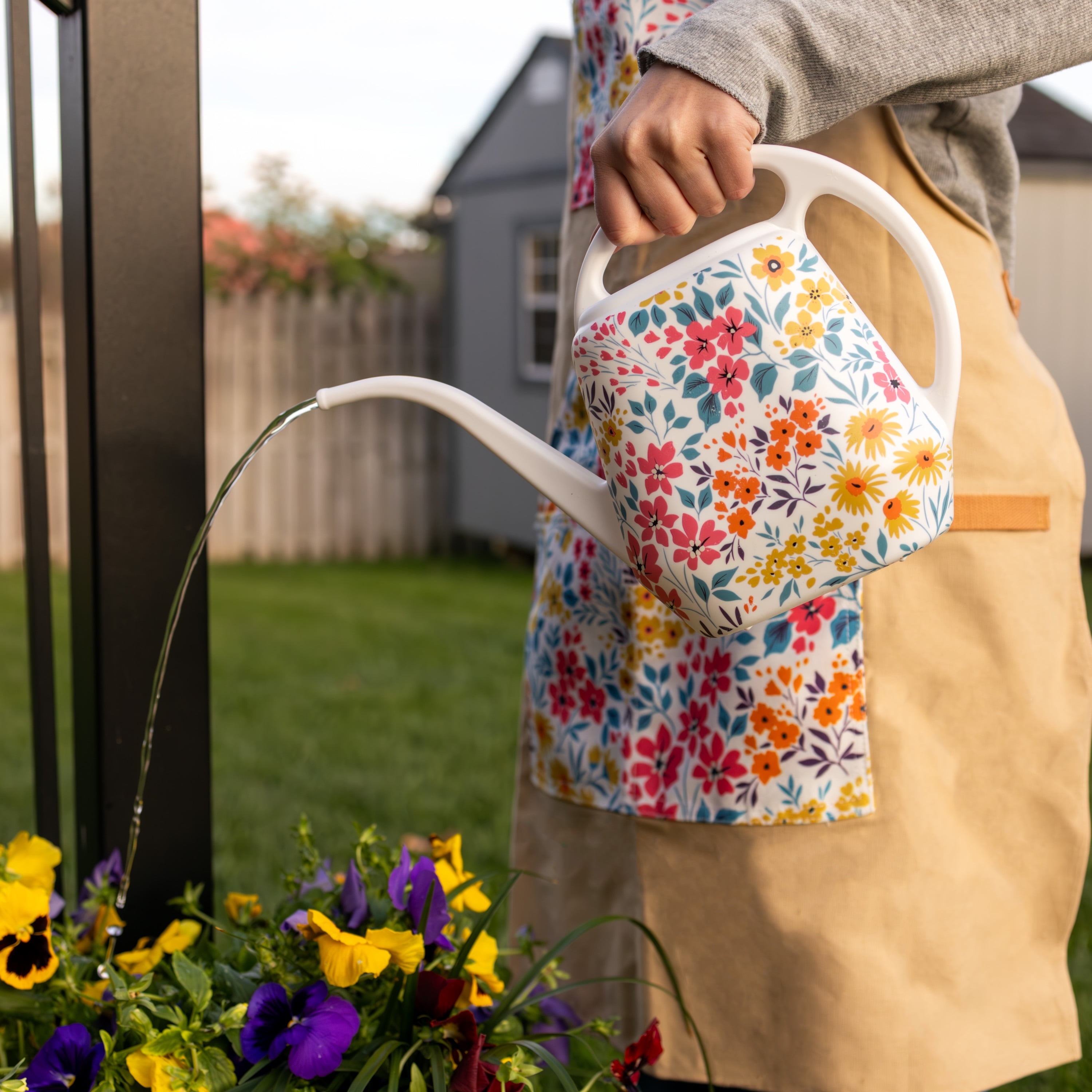 Person waters garden flowers with floral watering can in a backyard setting