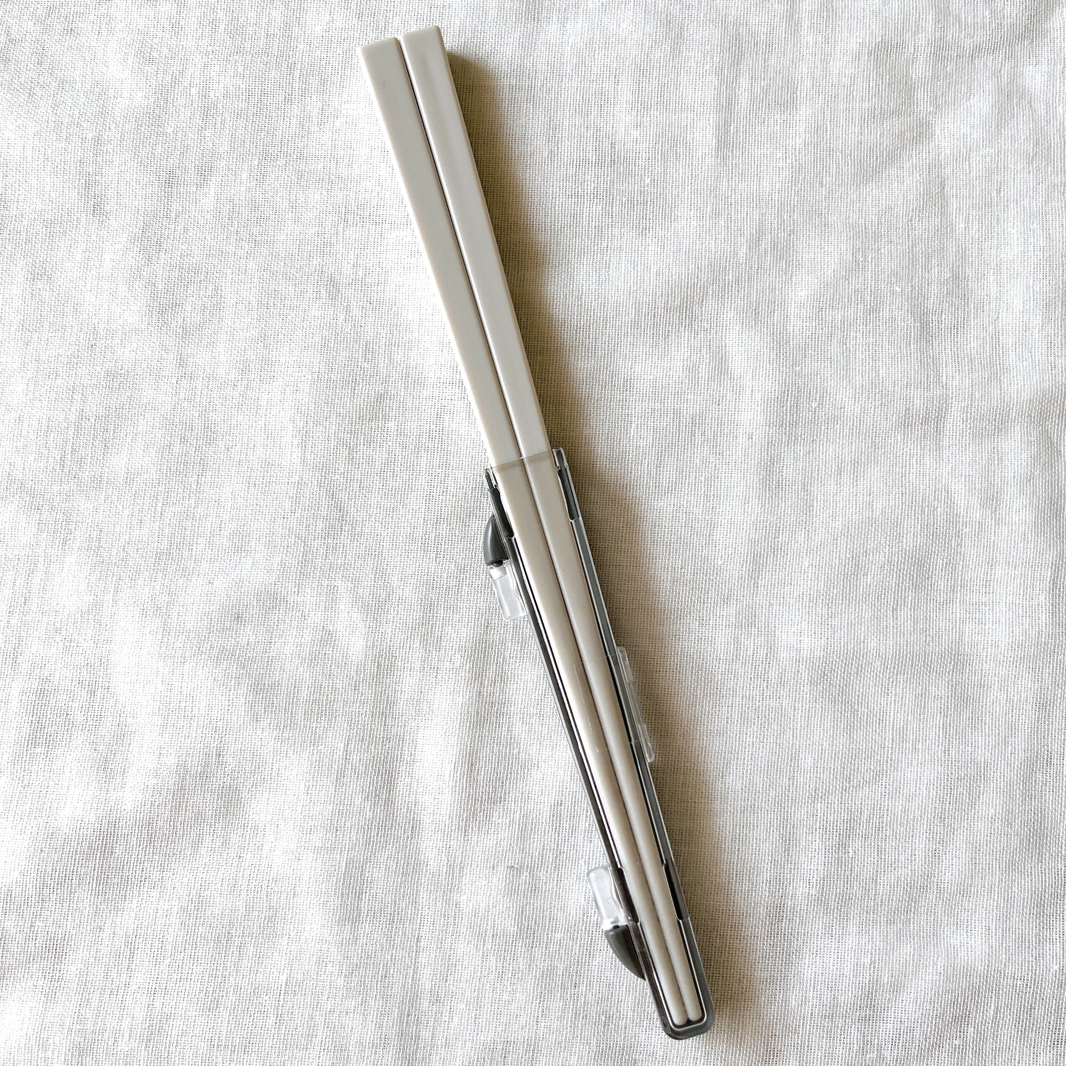 折りたたみ式の箸とケース。布の背景に置かれている。