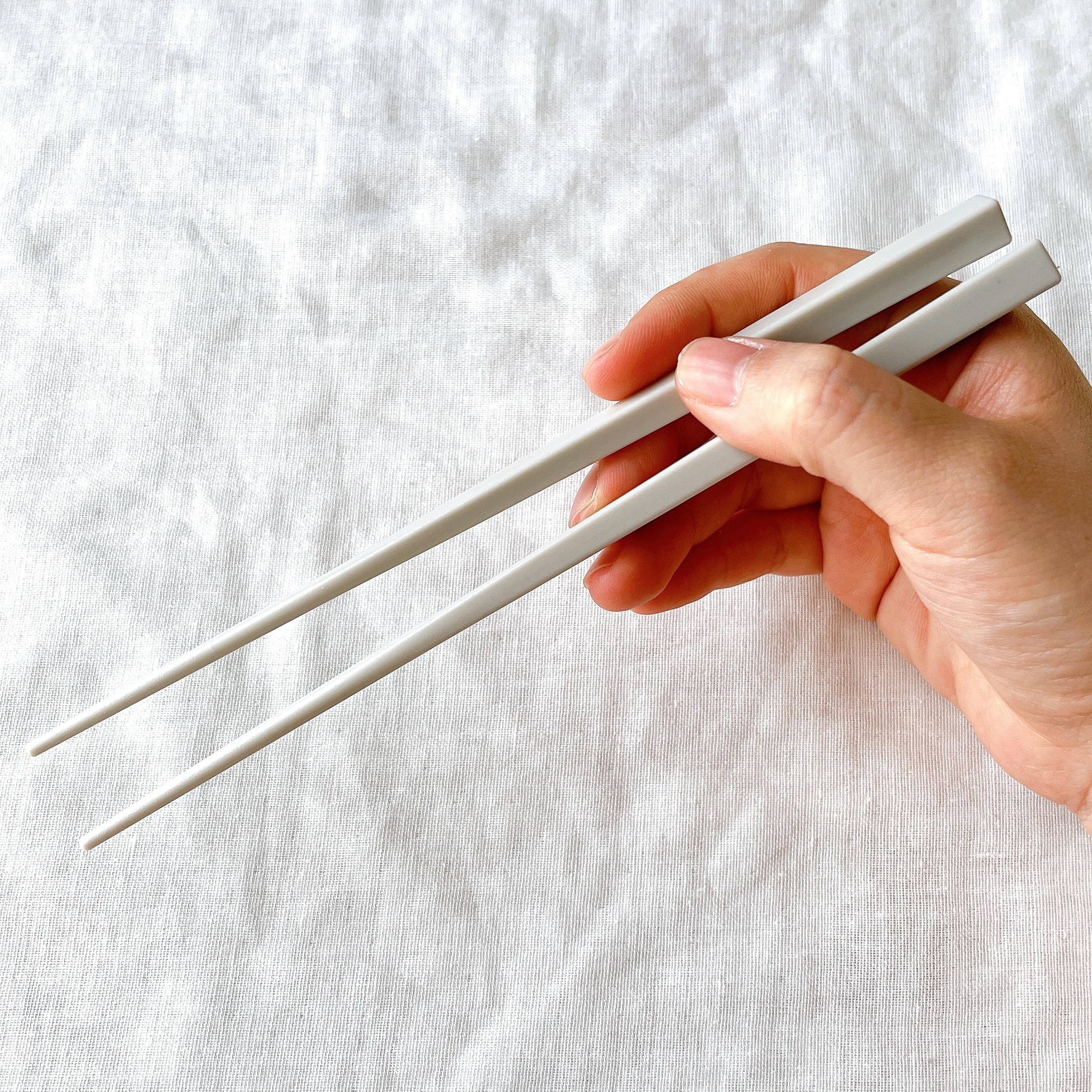 手が箸を持っている様子。背景は布地。