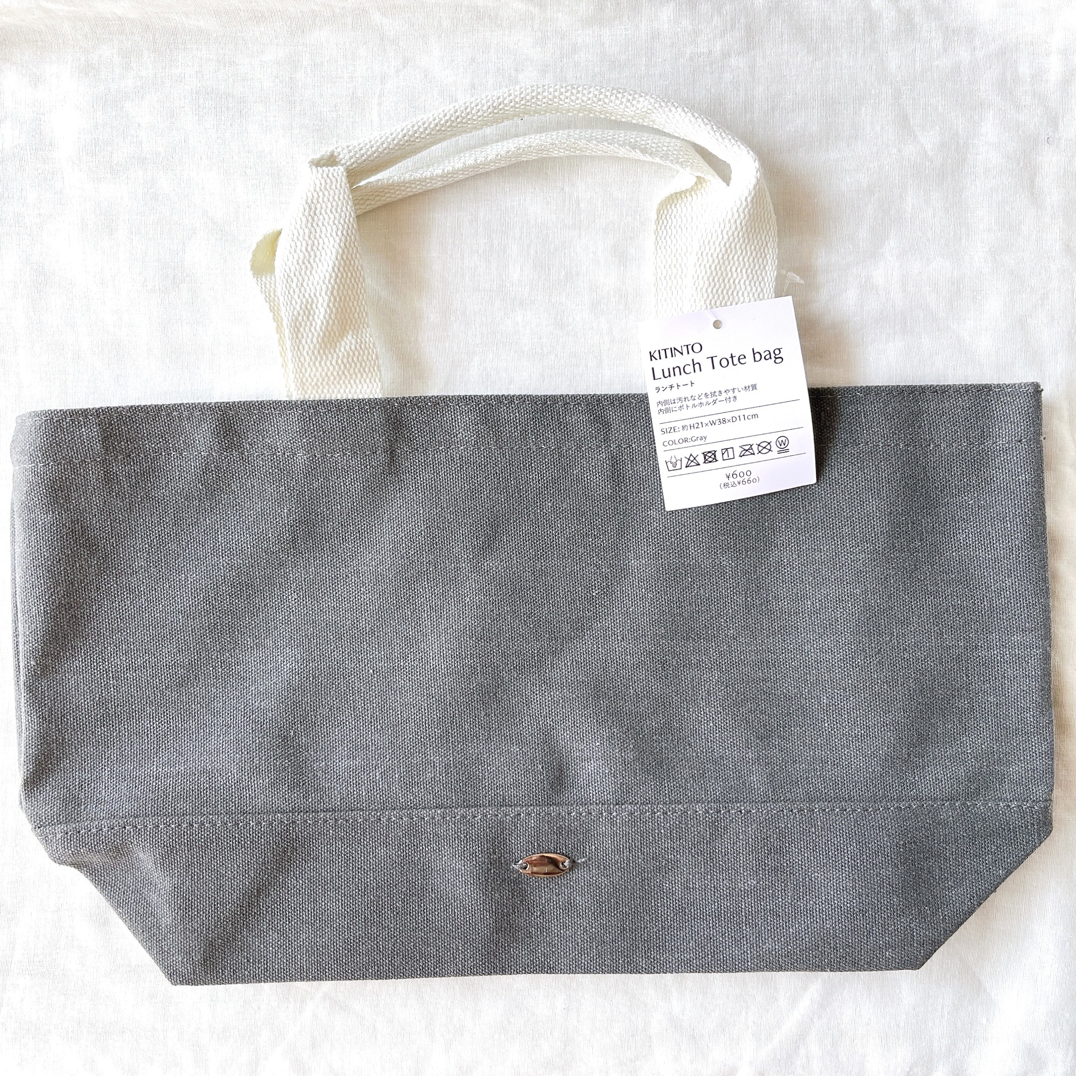 灰色のランチトートバッグに白い持ち手が付いており、価格タグが付いています。シンプルなデザインです。