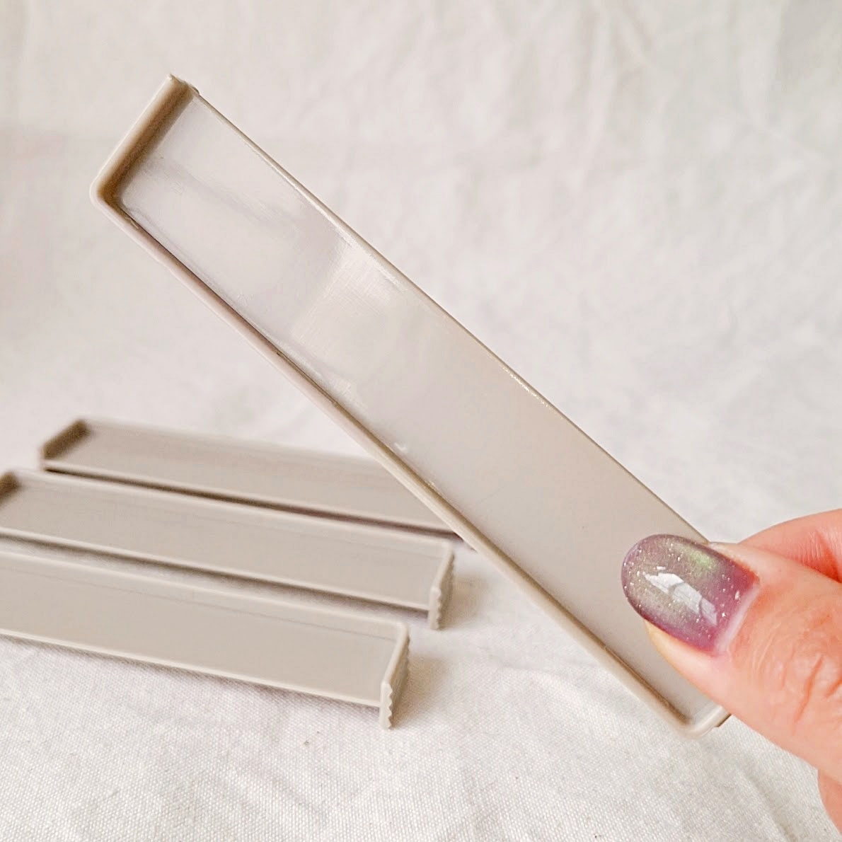 手に持たれた細長いプラスチックケースが、他の3つのケースと一緒に布の上に置かれています。