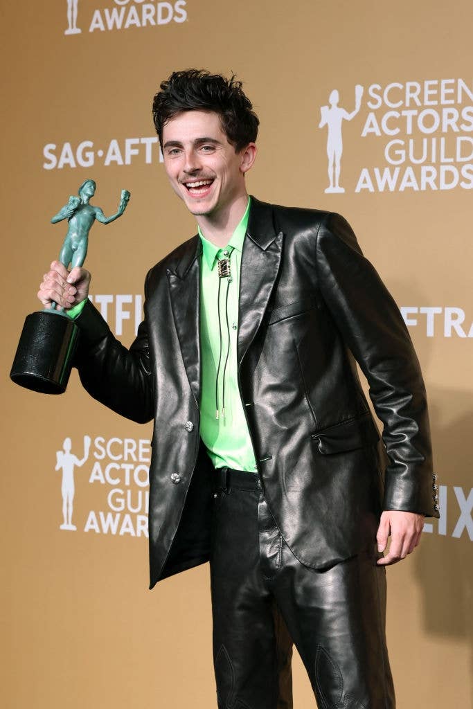 Person in a leather suit holding a Screen Actors Guild Award, smiling in front of an event backdrop