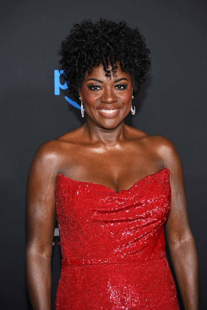 Woman in a strapless, sequined gown posing on a red carpet, smiling