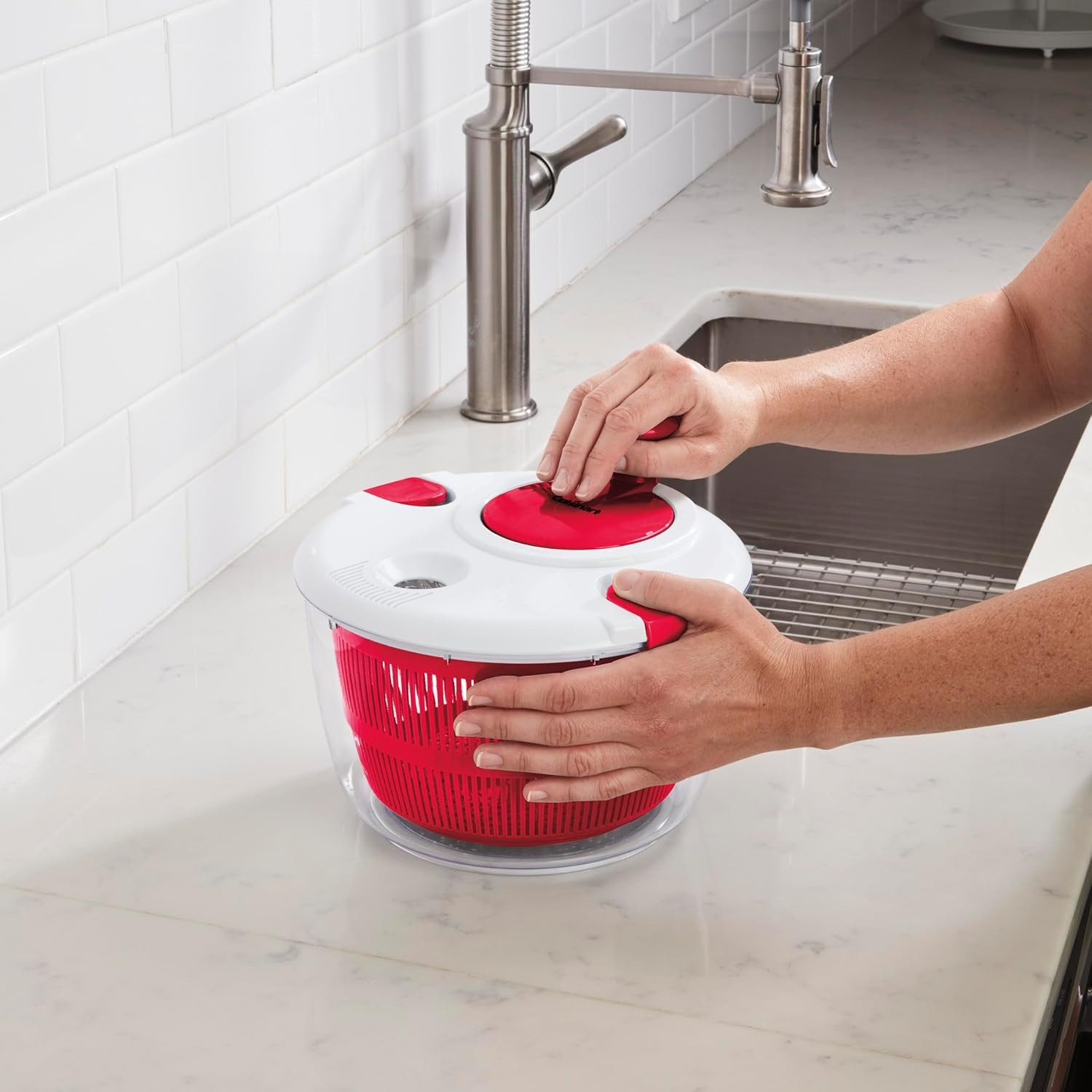 Person using a salad spinner with a red interior bowl on a kitchen counter