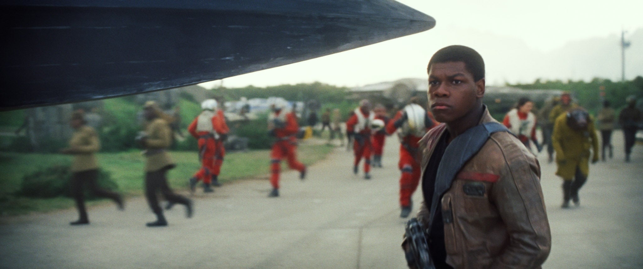 Actor in futuristic jacket on a sci-fi movie set, surrounded by crew members in pilot uniforms and bustling activity