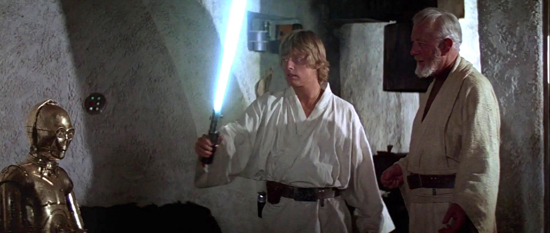 Scene from a sci-fi movie: A young man holds a glowing sword, watched by an elder in robes and a golden robot