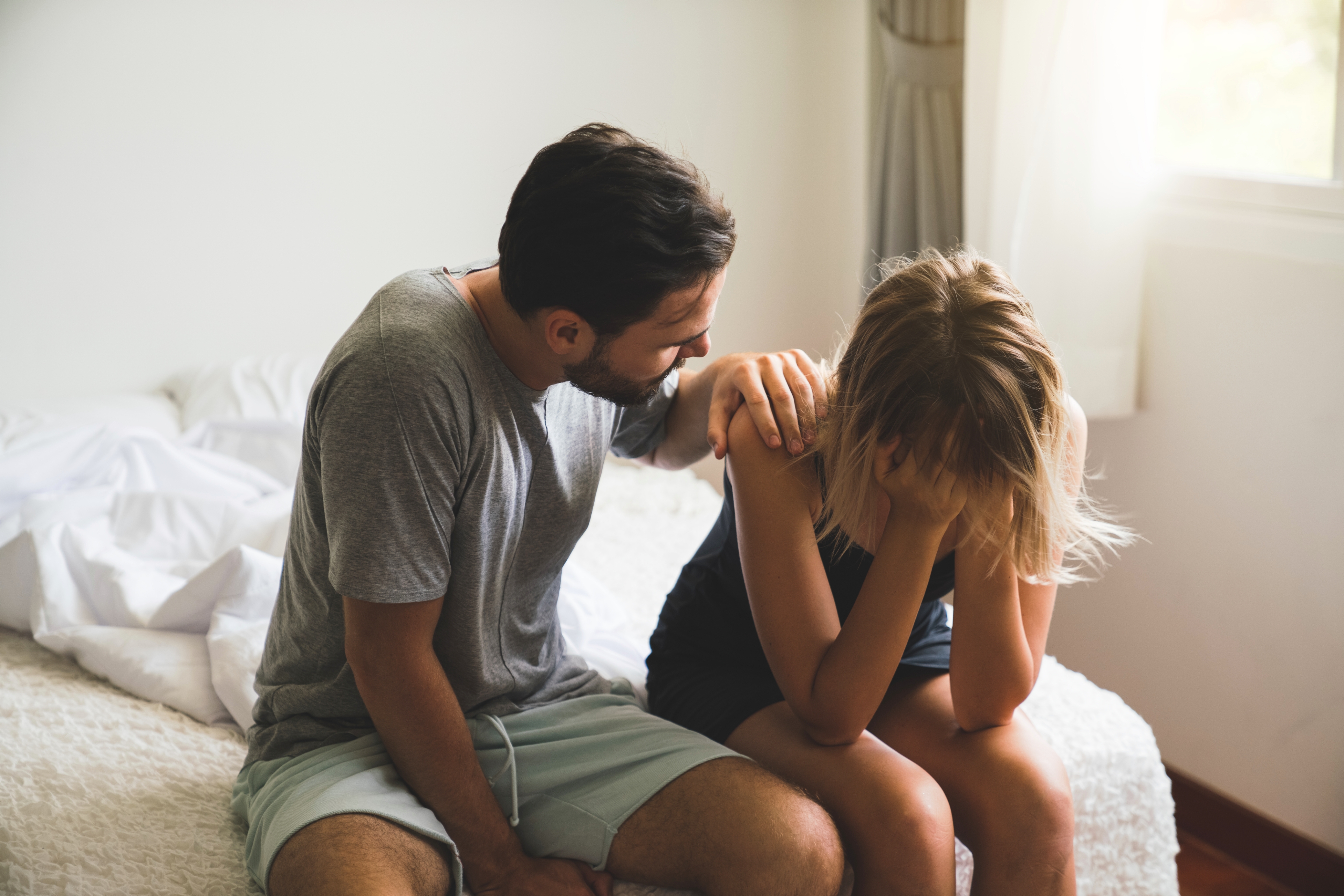 Man comforts woman sitting on bed, showing empathy and support in a moment of emotional distress