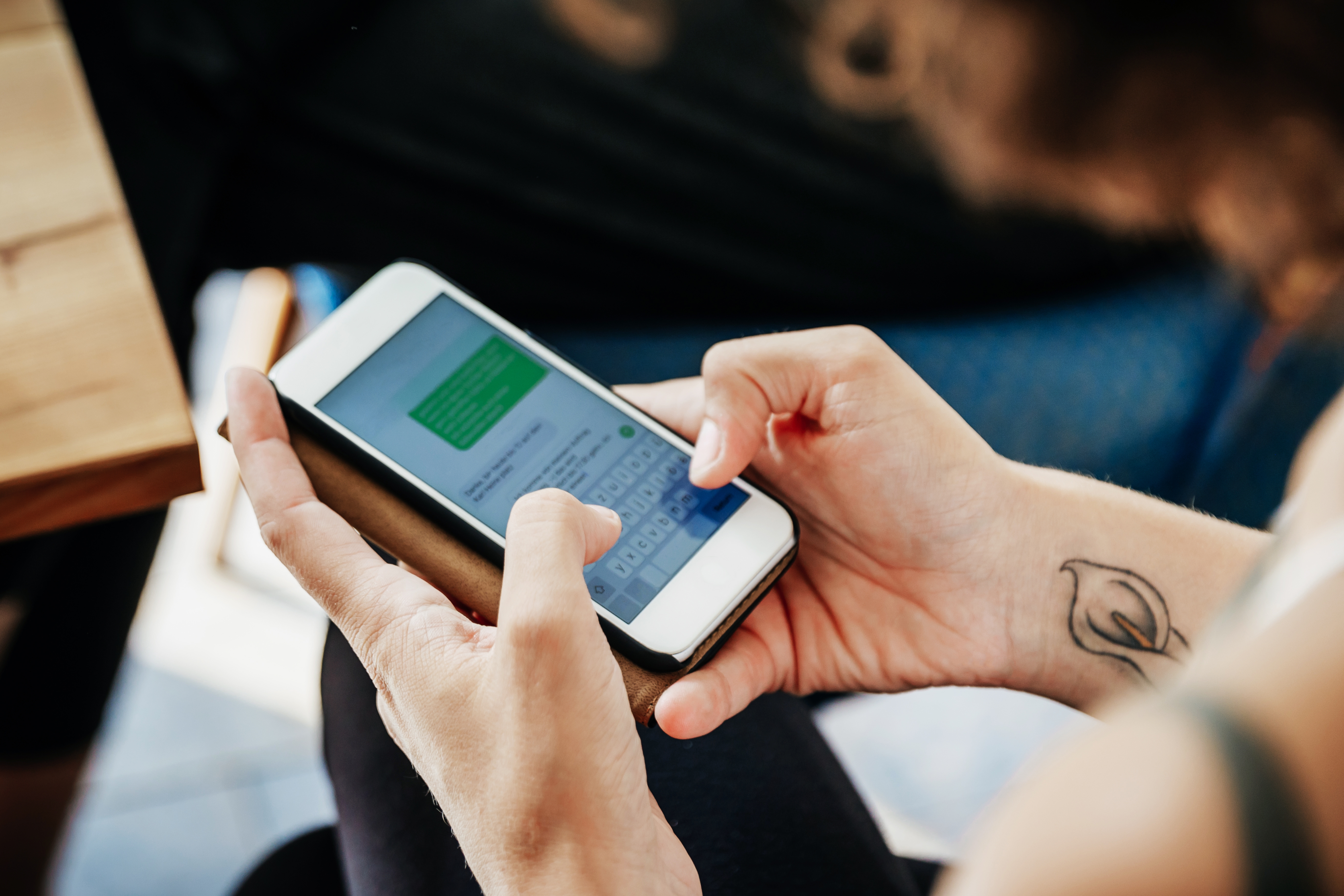 En person som skriver en melding på en smarttelefon, synlig tatovering på håndleddet, og komponerer et tekst svar