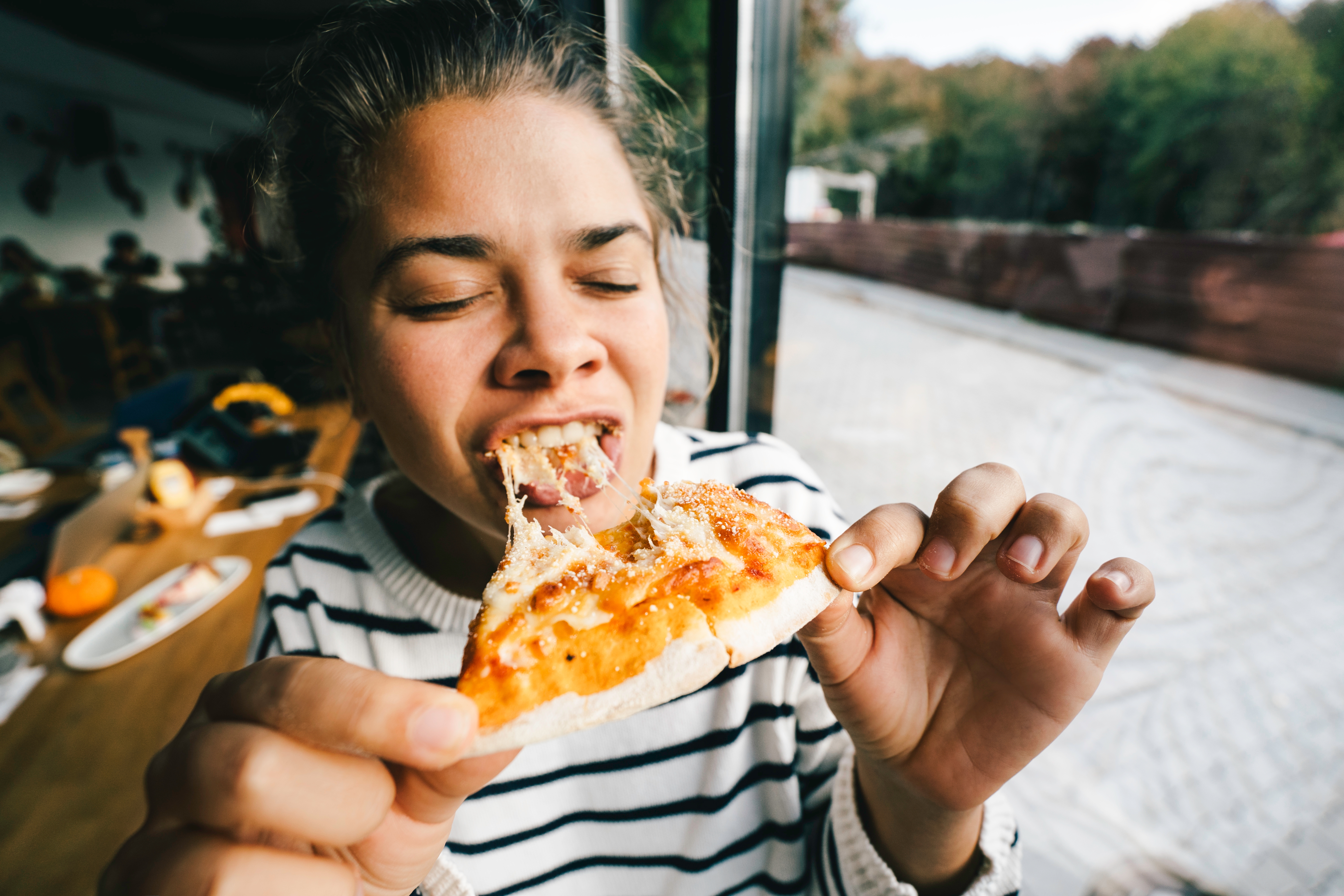Person med glede å spise en skive pizza ved et bord ved et vindu, ha på seg en stripet skjorte