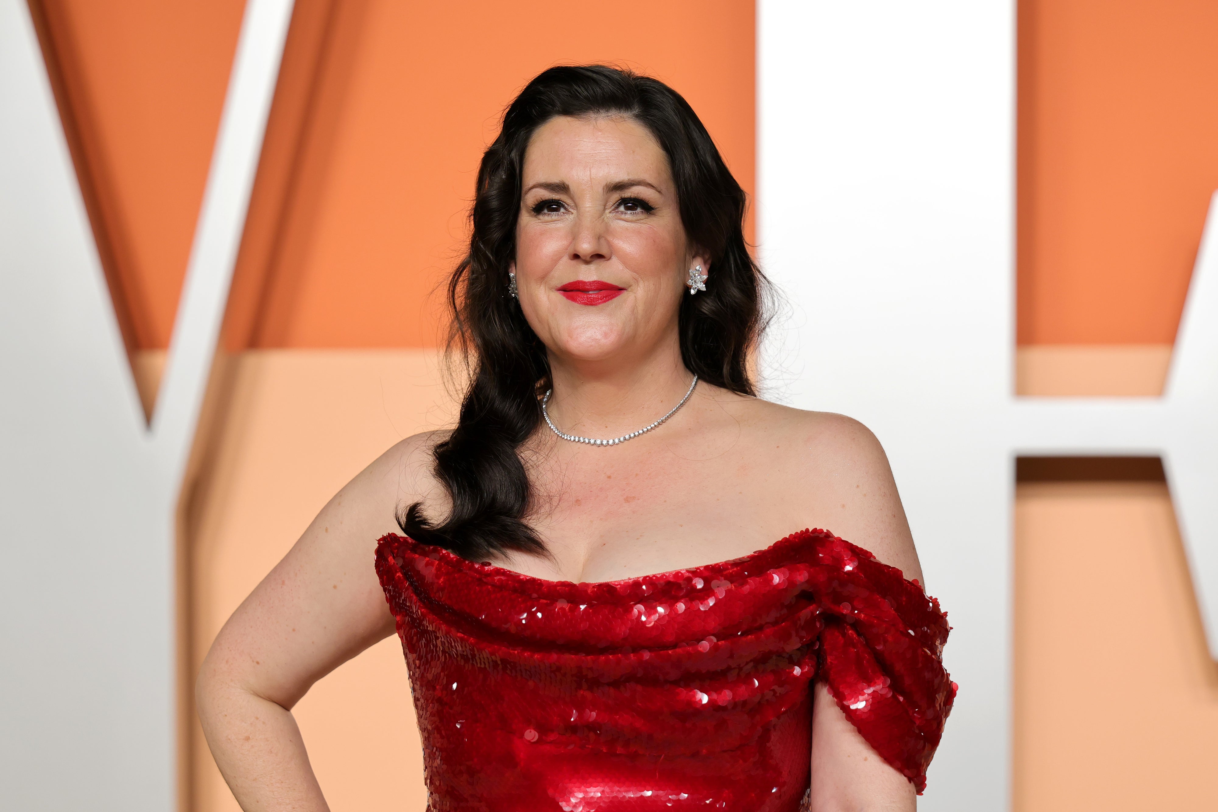Person in an off-shoulder sequined gown poses confidently on the red carpet