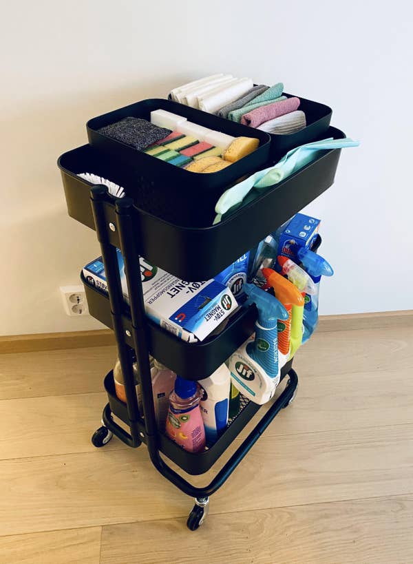 A RÅSKOG trolley filled with organized cleaning supplies, including spray bottles and cloths, showcasing a DIY storage solution. Reddit page visible in the background