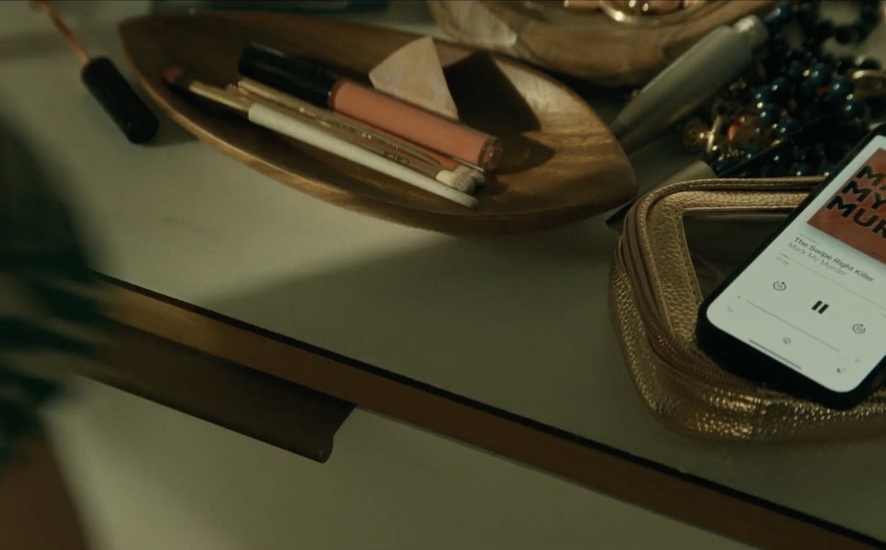 Smartphone on a table with the "Mark My Murder" podcast playing.