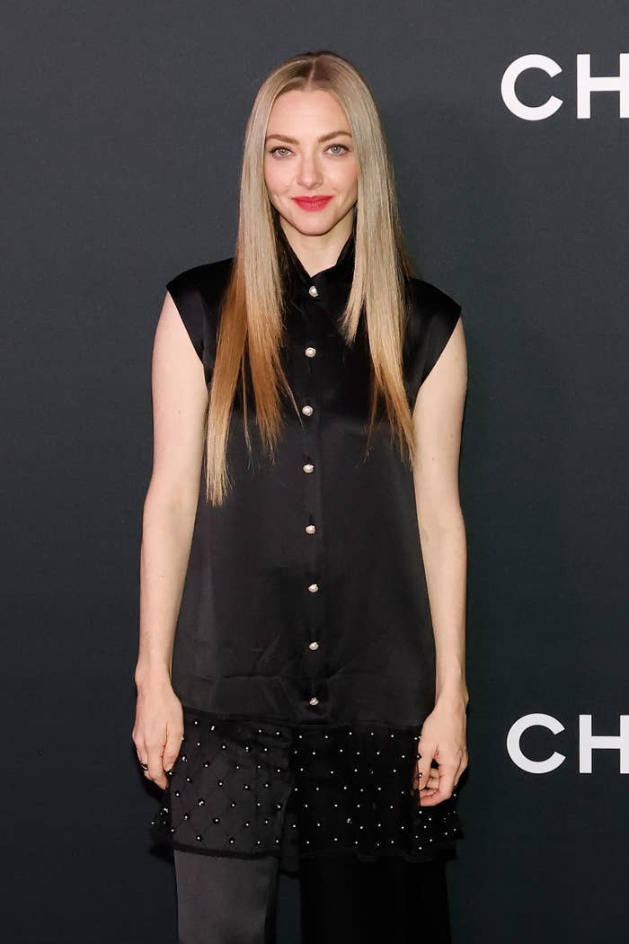 Person in a sleeveless, button-up black outfit with long straight hair, standing indoors at an event
