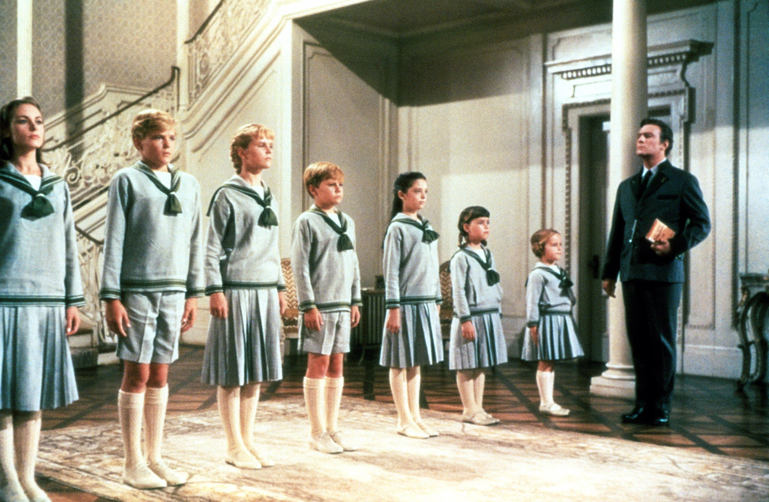 Seven children in matching sailor outfits stand in a row
