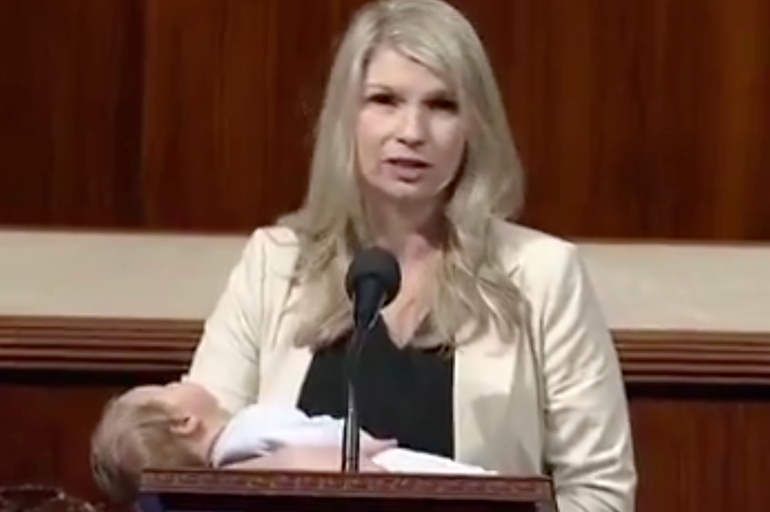 女性が赤ちゃんを抱きながら演壇で話している様子。