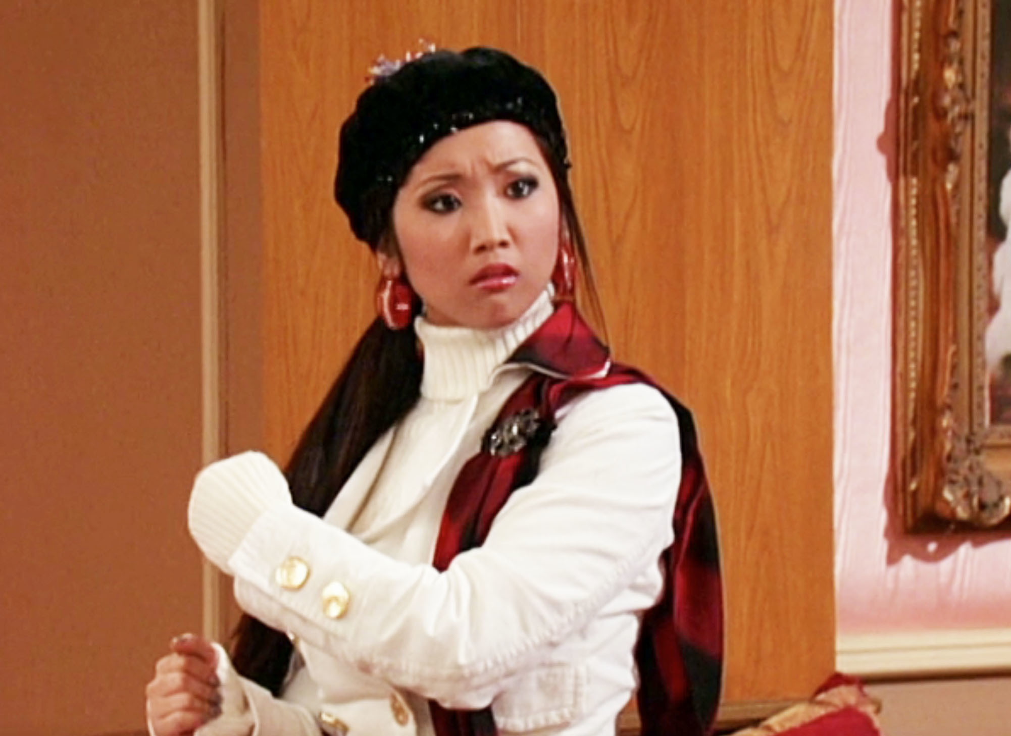 Person in a stylish beret and white jacket with gold buttons looking surprised on a TV show set