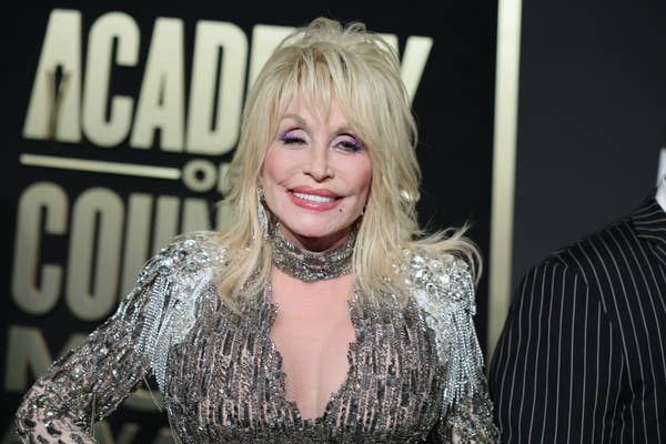 A person smiling at an event, wearing a sequin-embellished dress with intricate details. The background shows "Academy of Country Music."